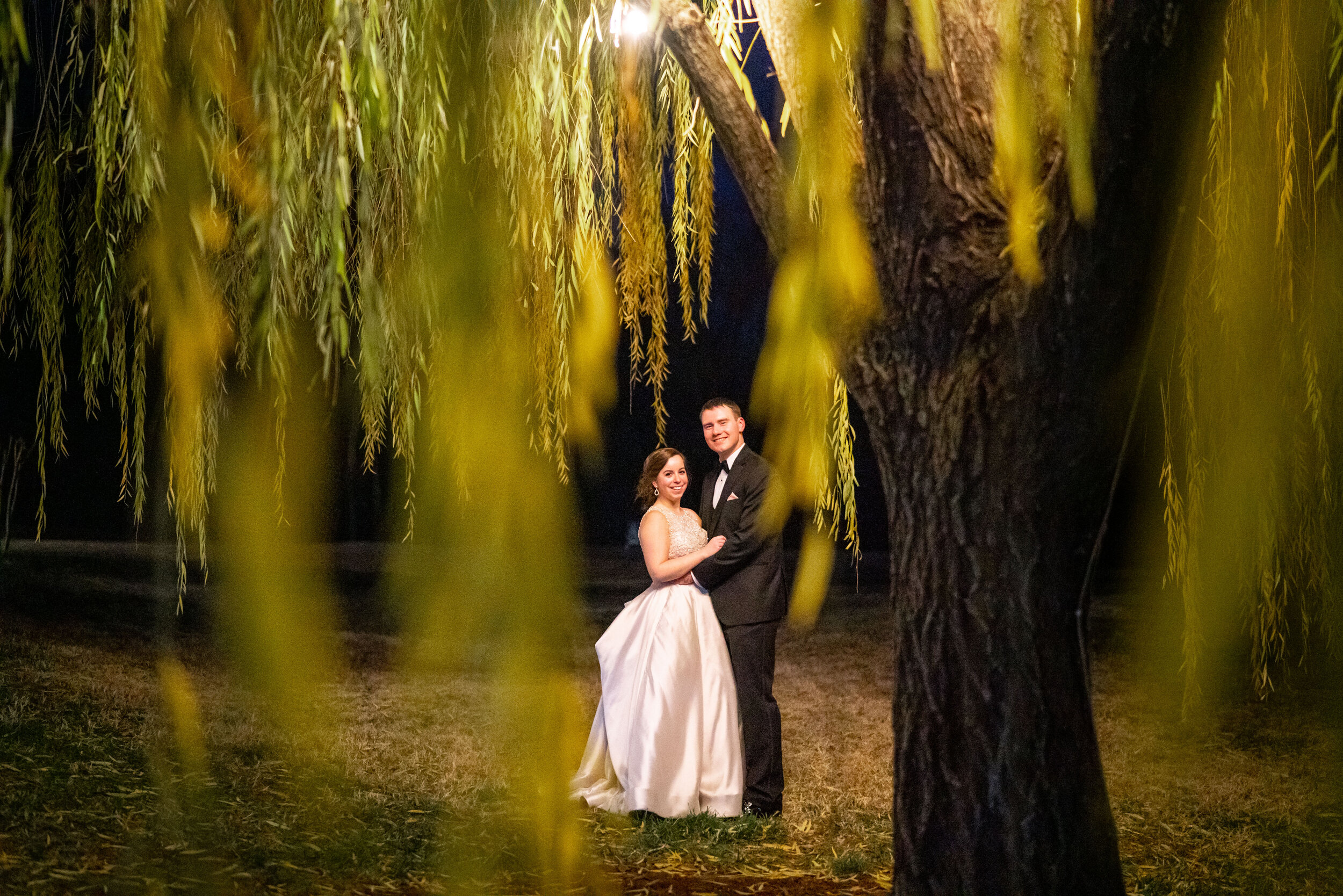Night portrait of bride and groom under the willow tree behind Ospreys at Belmont Bay