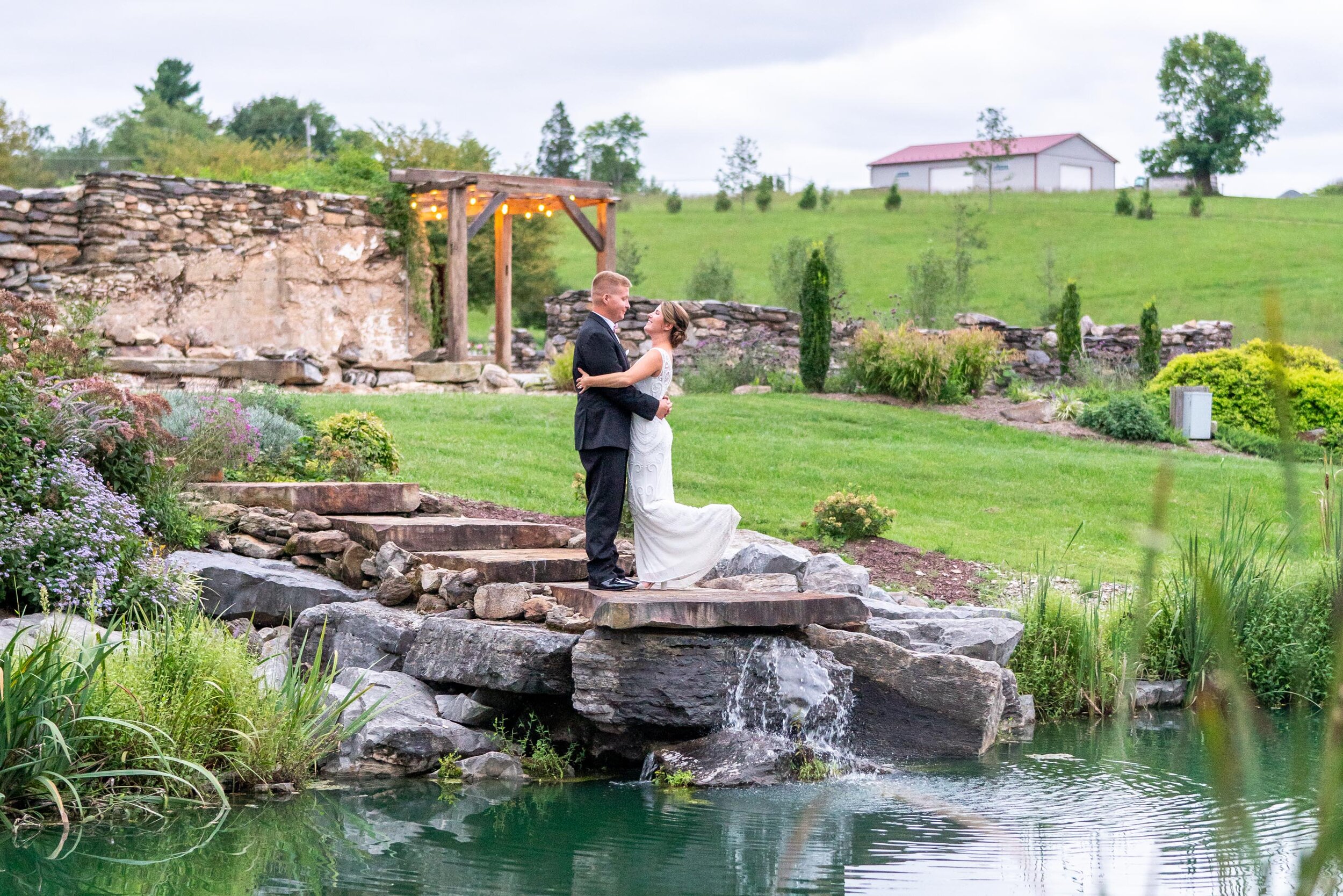 Bride and groom on rock ledge over pond lake at Glen Ellen Farm venue
