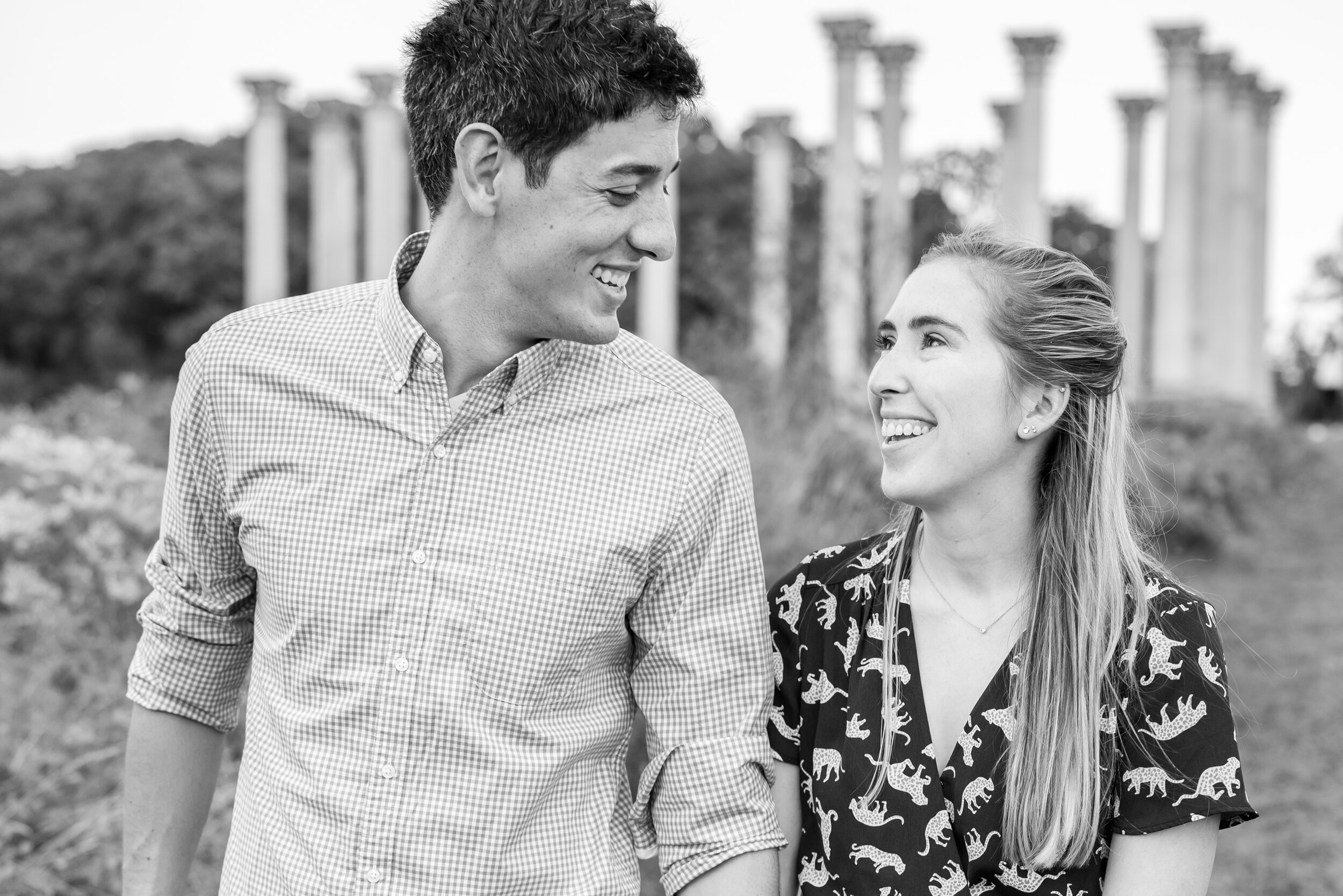 Engaged couple looking at each other smiling in front of columns National Arboretum