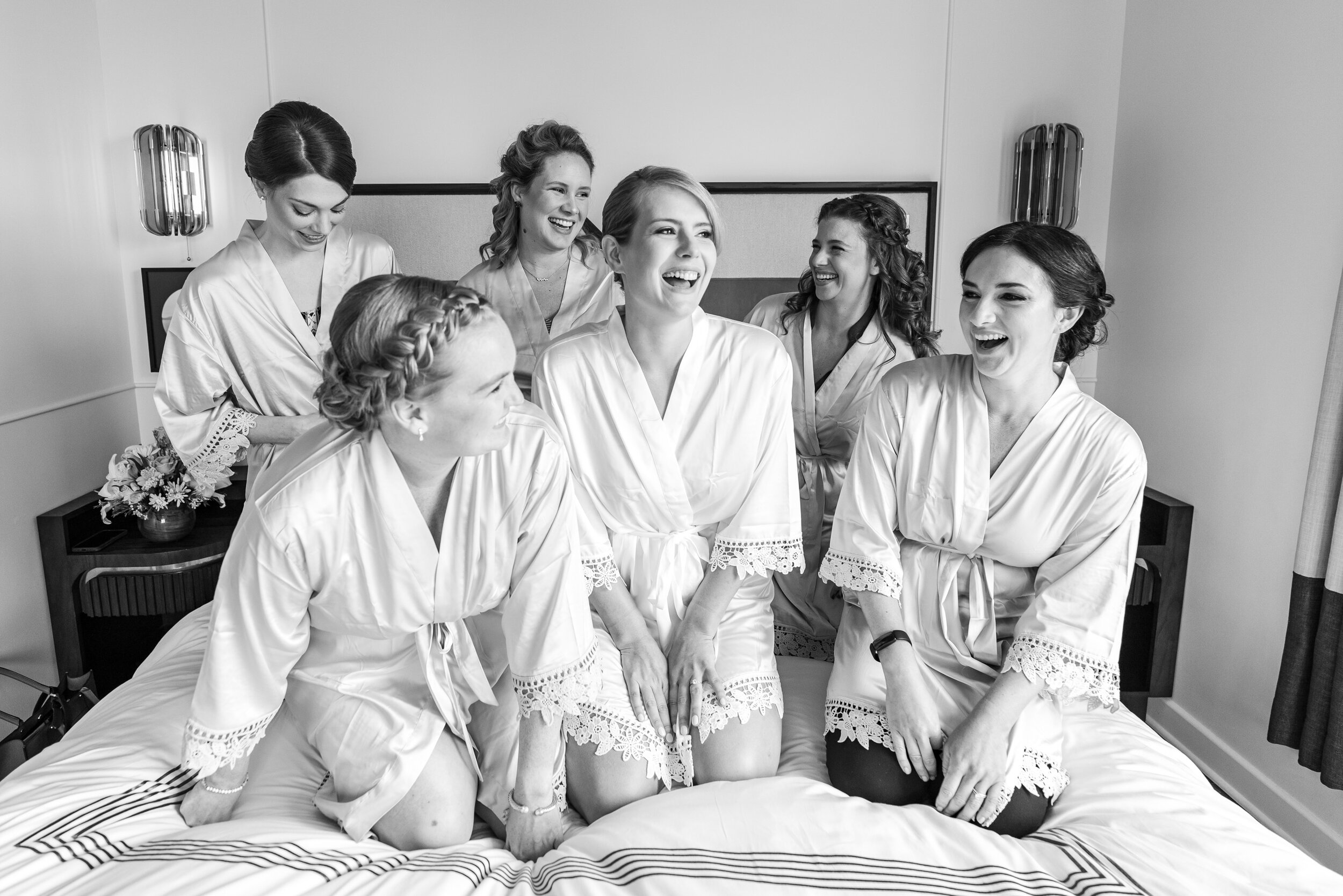 Bride and bridesmaids laughing on bed at Thompson Hyatt in DC