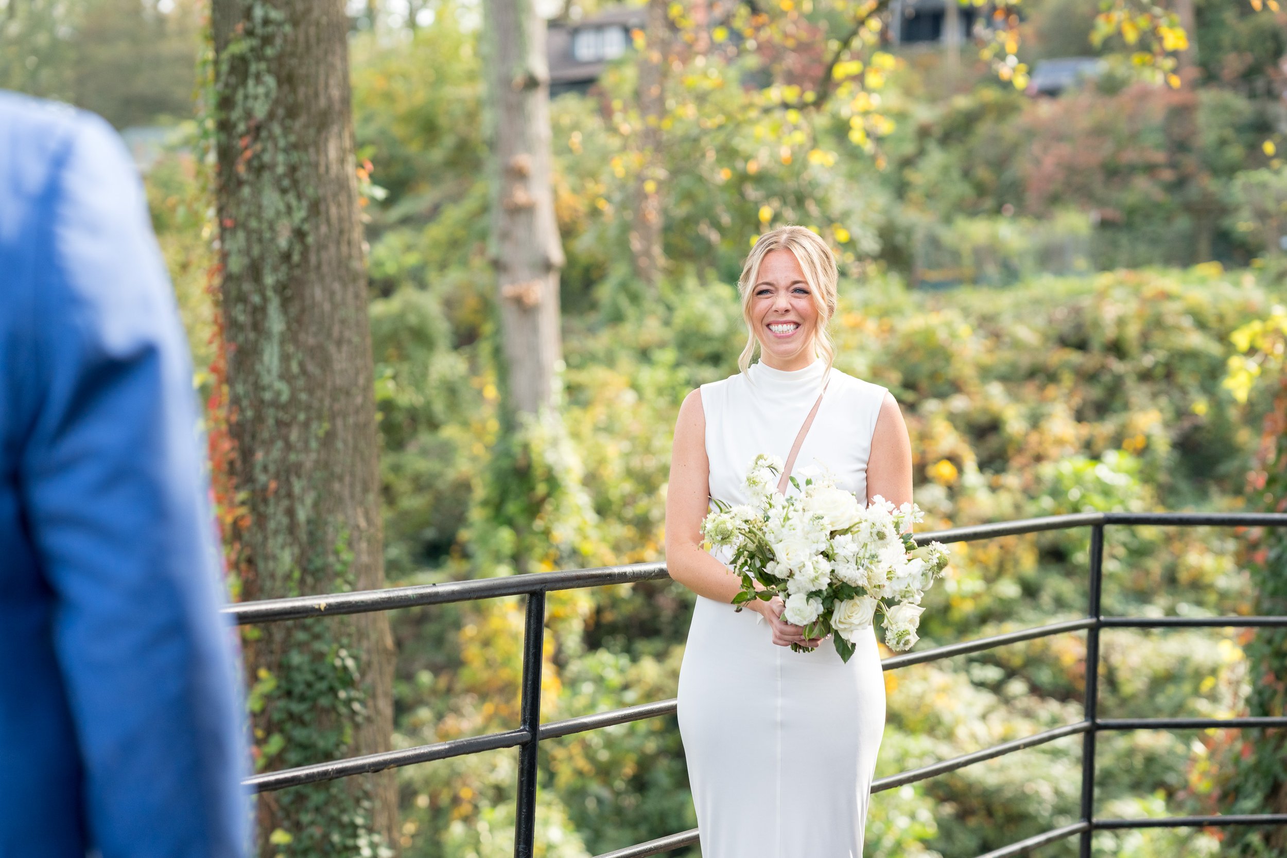 Bride smiles at groom holding flowers wearing white Tom Ford wedding dress
