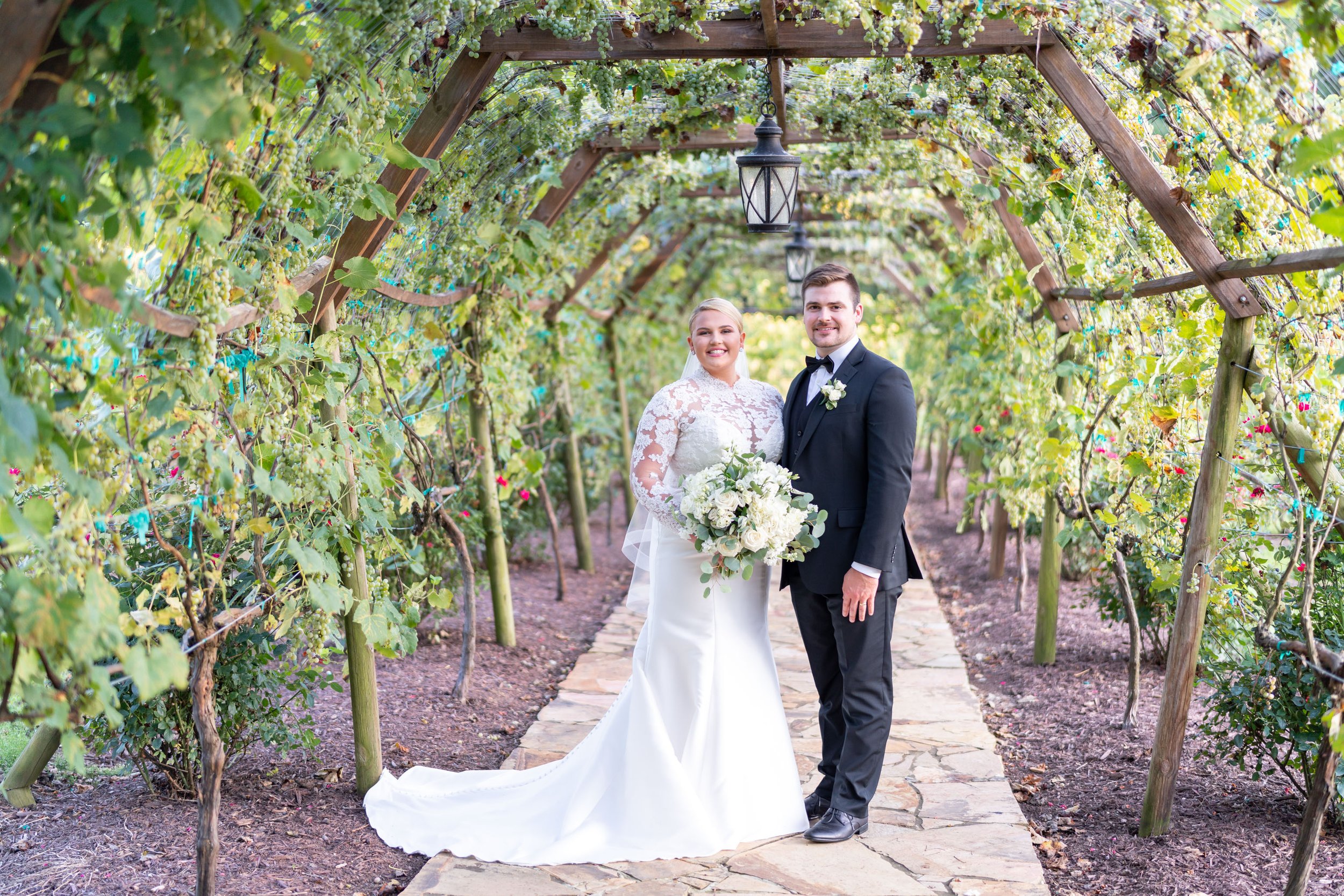 Bride and groom pose under rose grape archway at Running Hare Vineyard