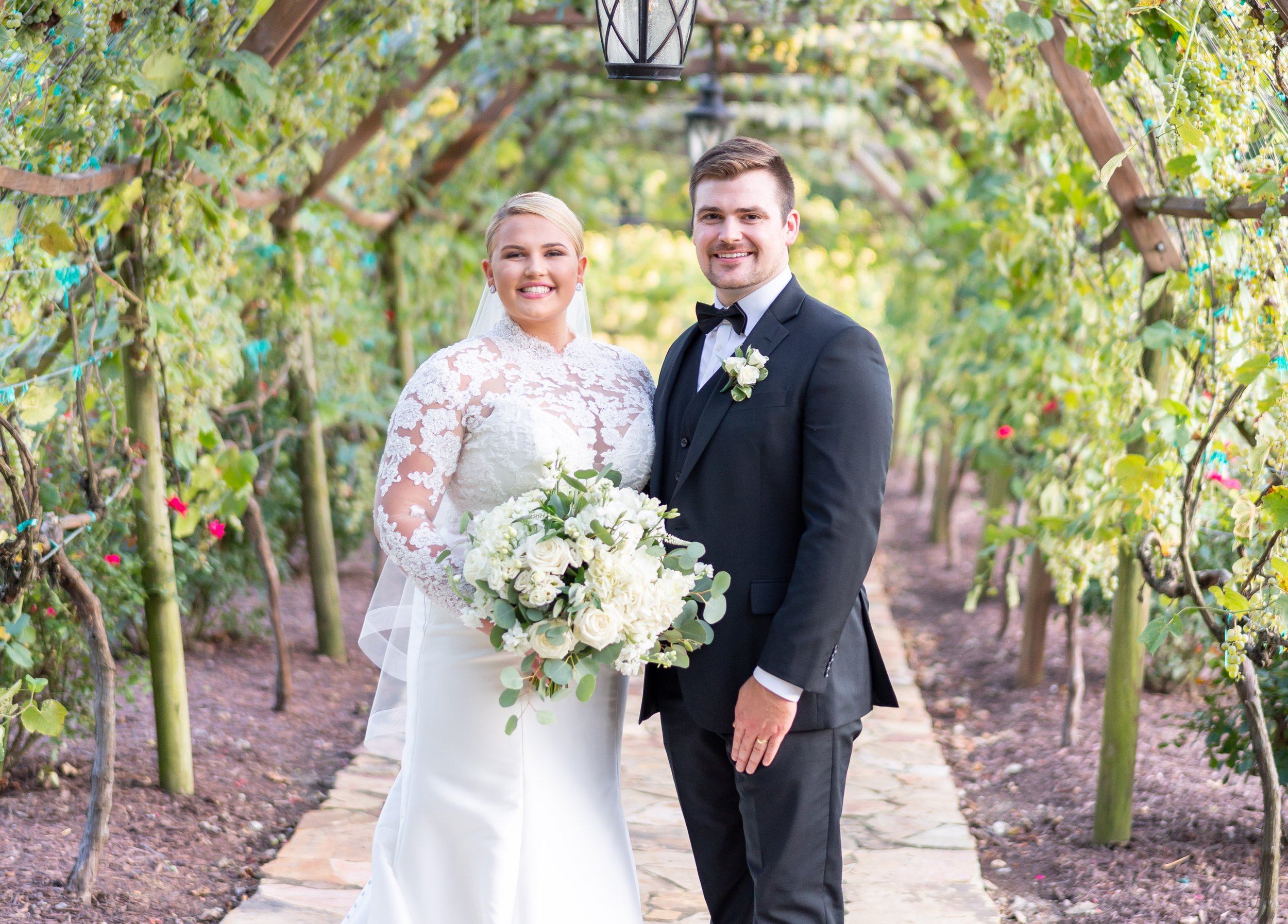 bride and groom pose smiling under vine archway at running hare vineyard