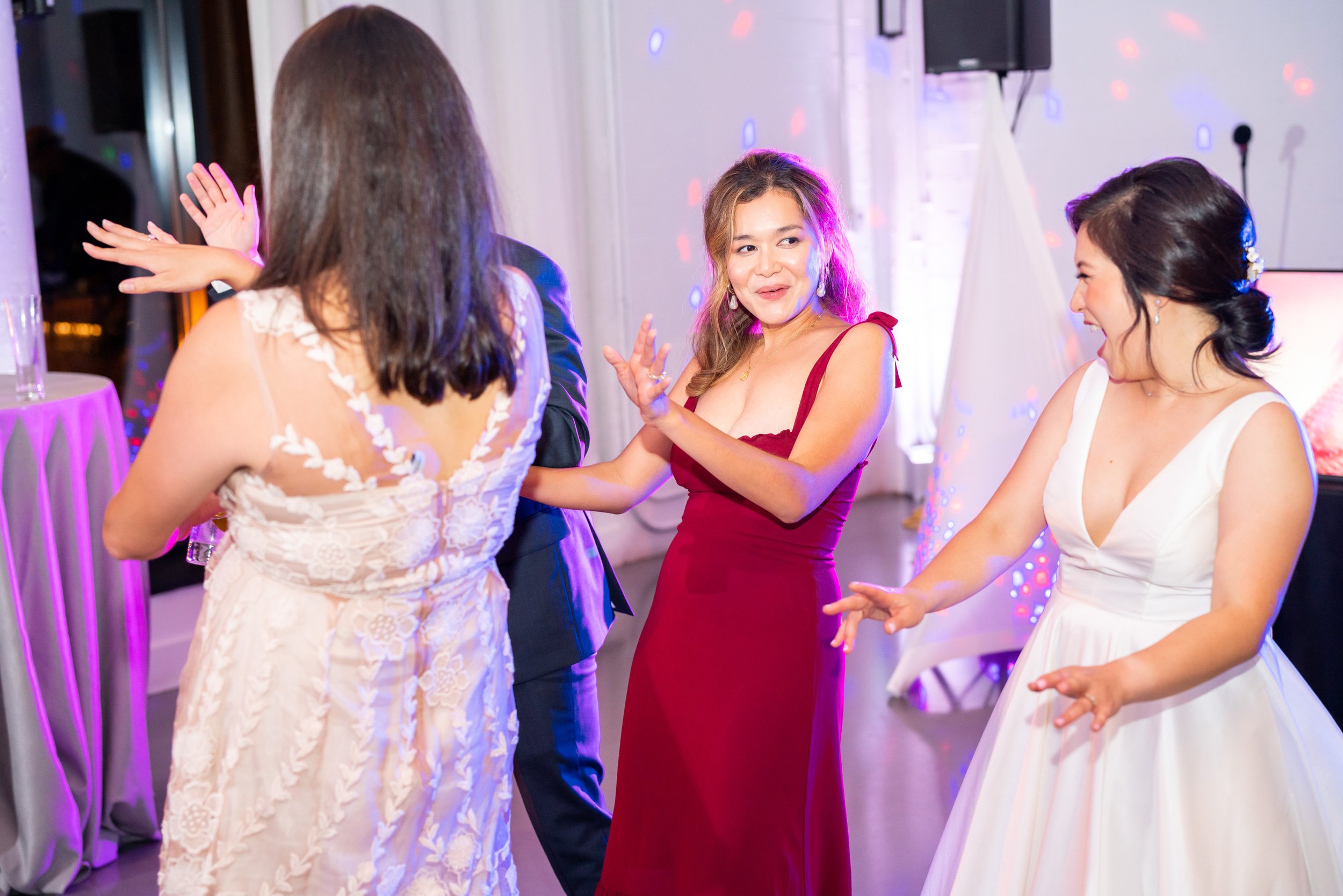 Bride dances with guests on colorful dance floor with purple uplighting 