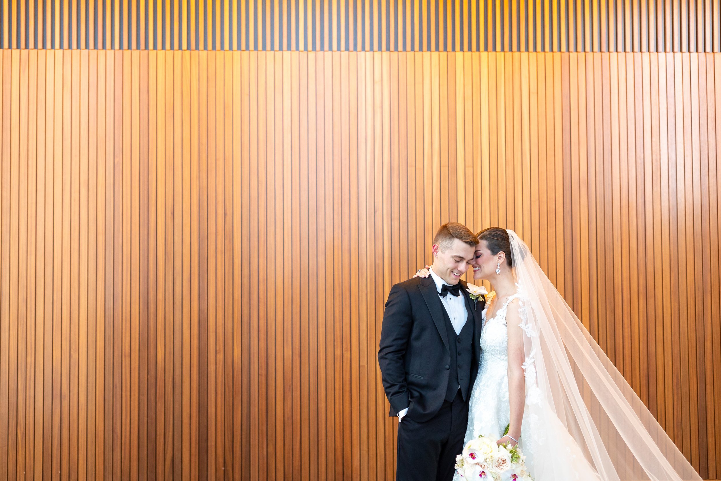 Bride and groom snuggle against wooden wall at Capital One Hall wedding ceremony space