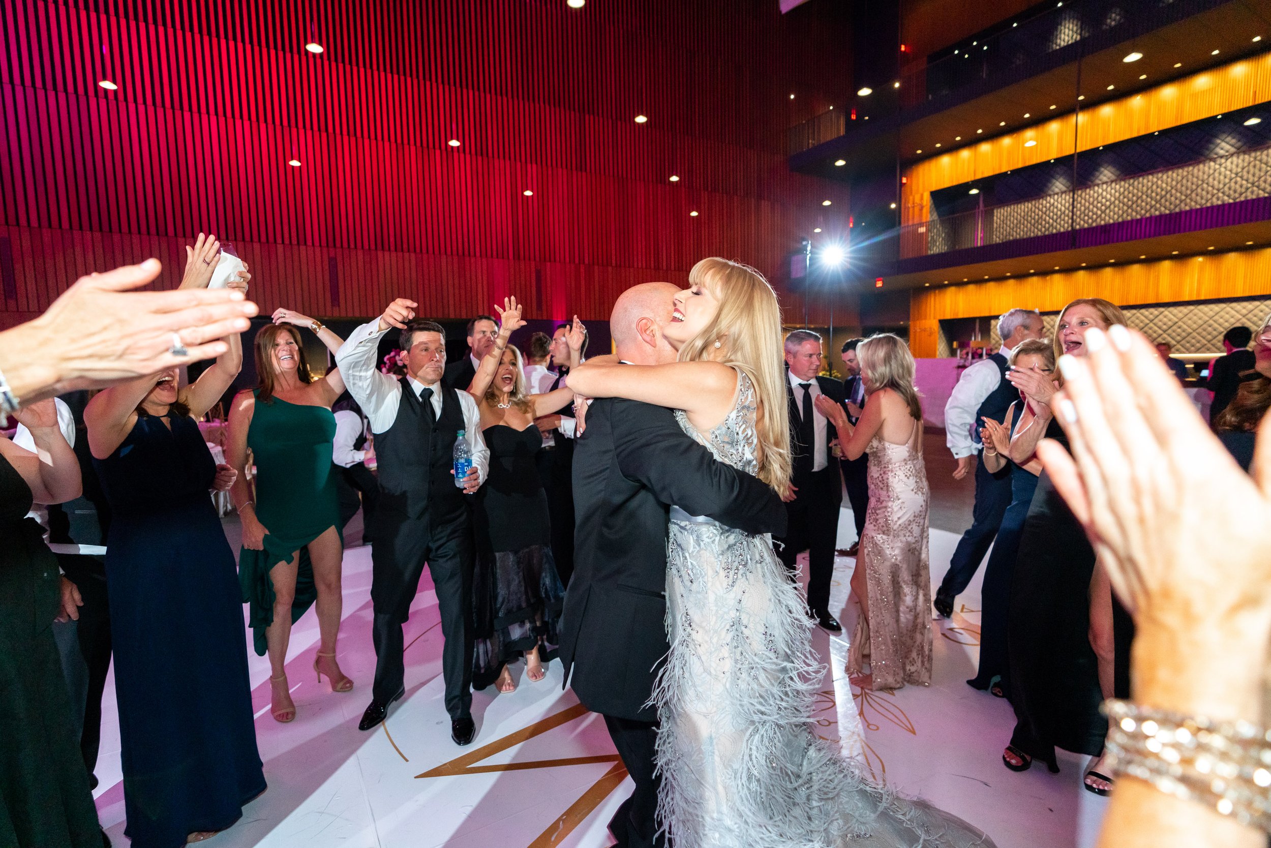 Parents of the bride spin and kiss on the dance floor surrounded by guests