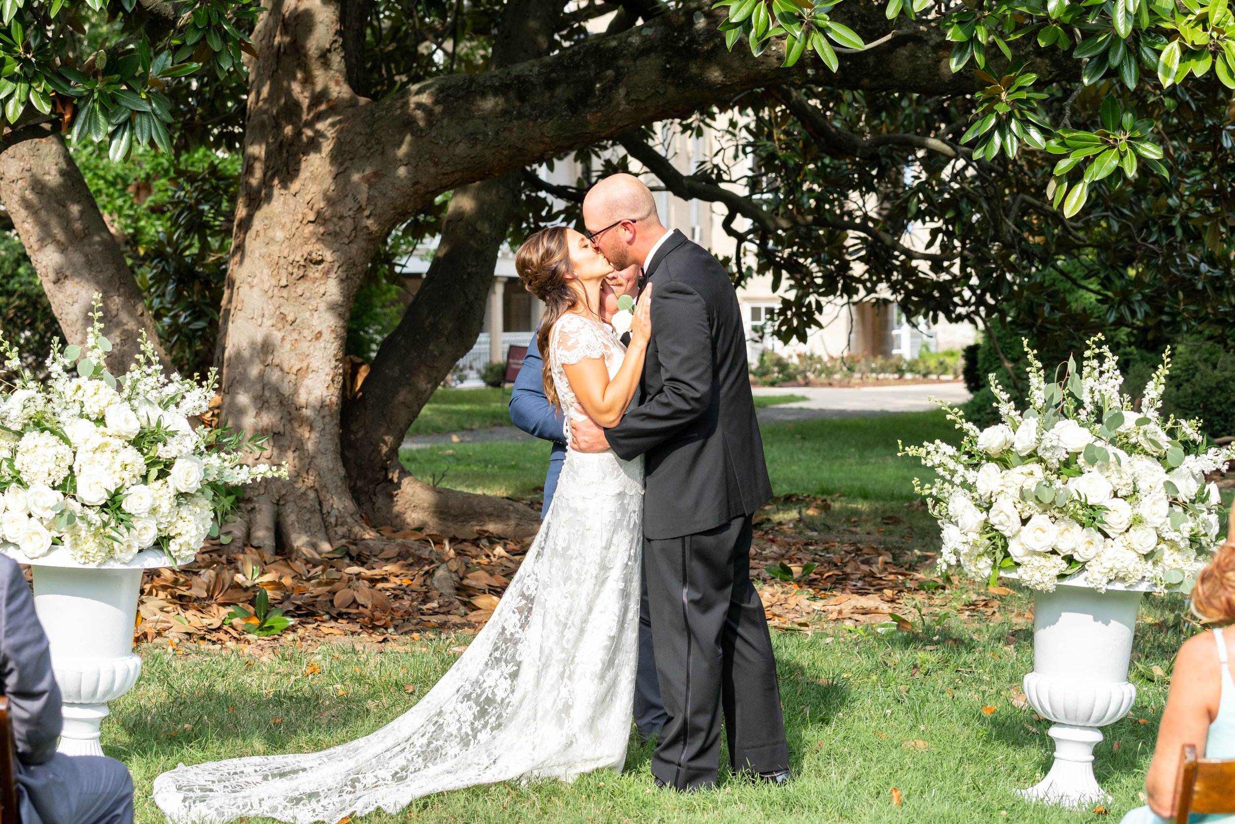 Bride and groom kiss at outdoor wedding ceremony under magnolia tree at Lincolns Cottage 