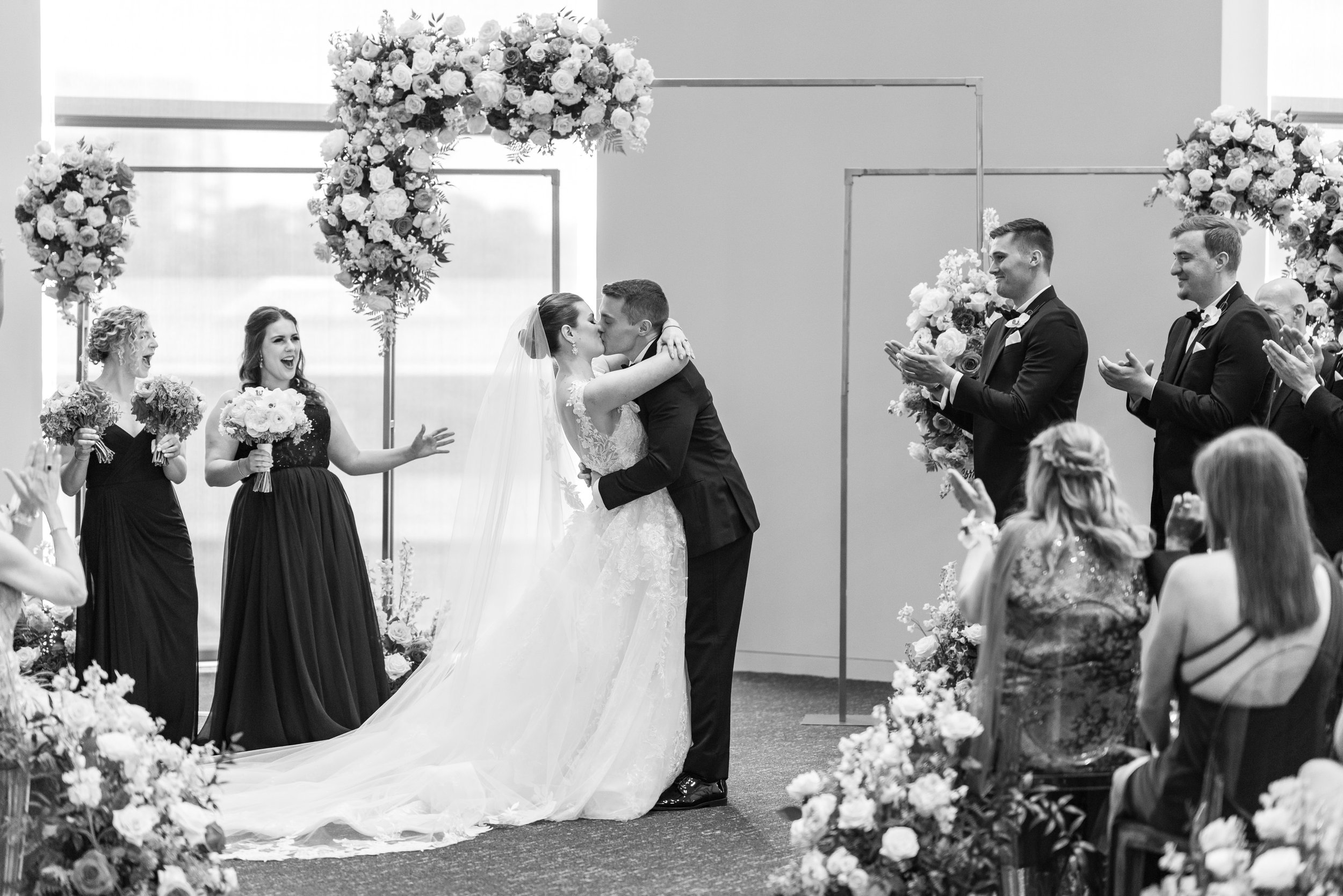 Bride and groom kiss at ceremony while bridesmaids cheer