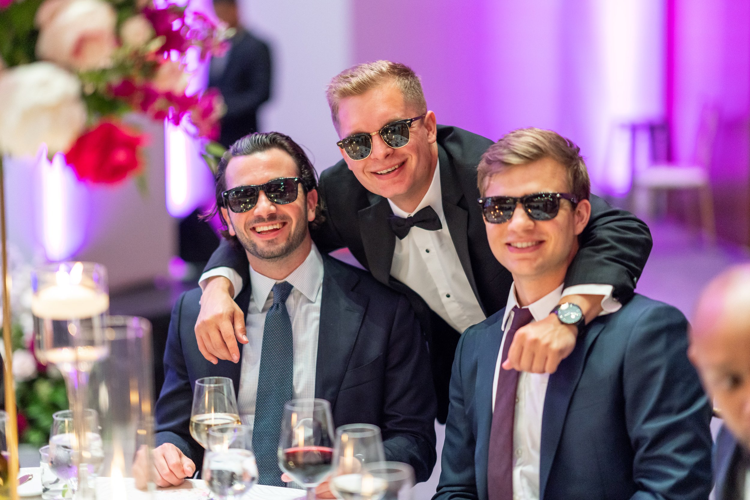 Three wedding guests laugh and smile for camera in sunglasses at wedding reception candids
