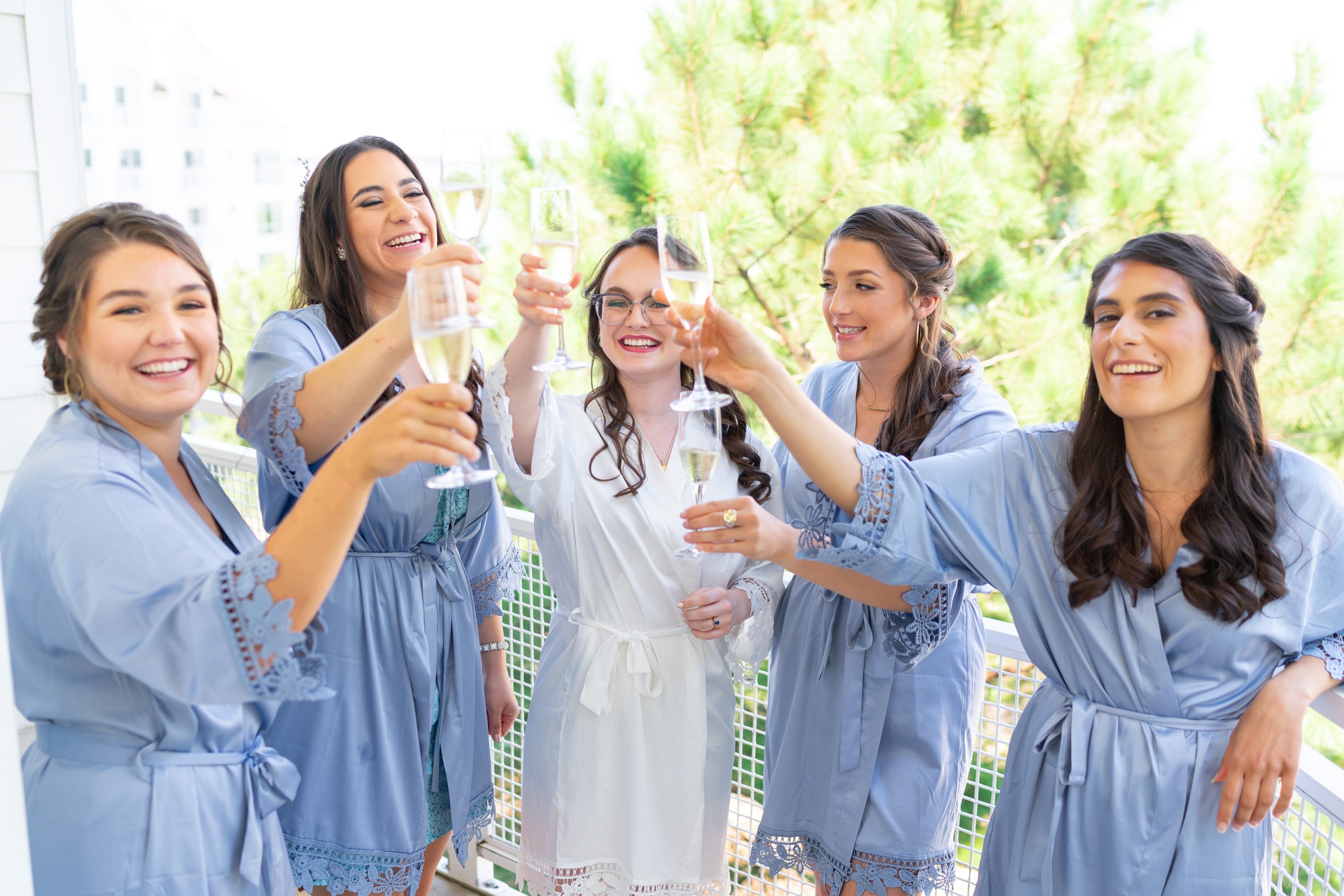 Bride and bridesmaids in matching blue silk robes toast champagne on balcony at Hyatt Chesapeake