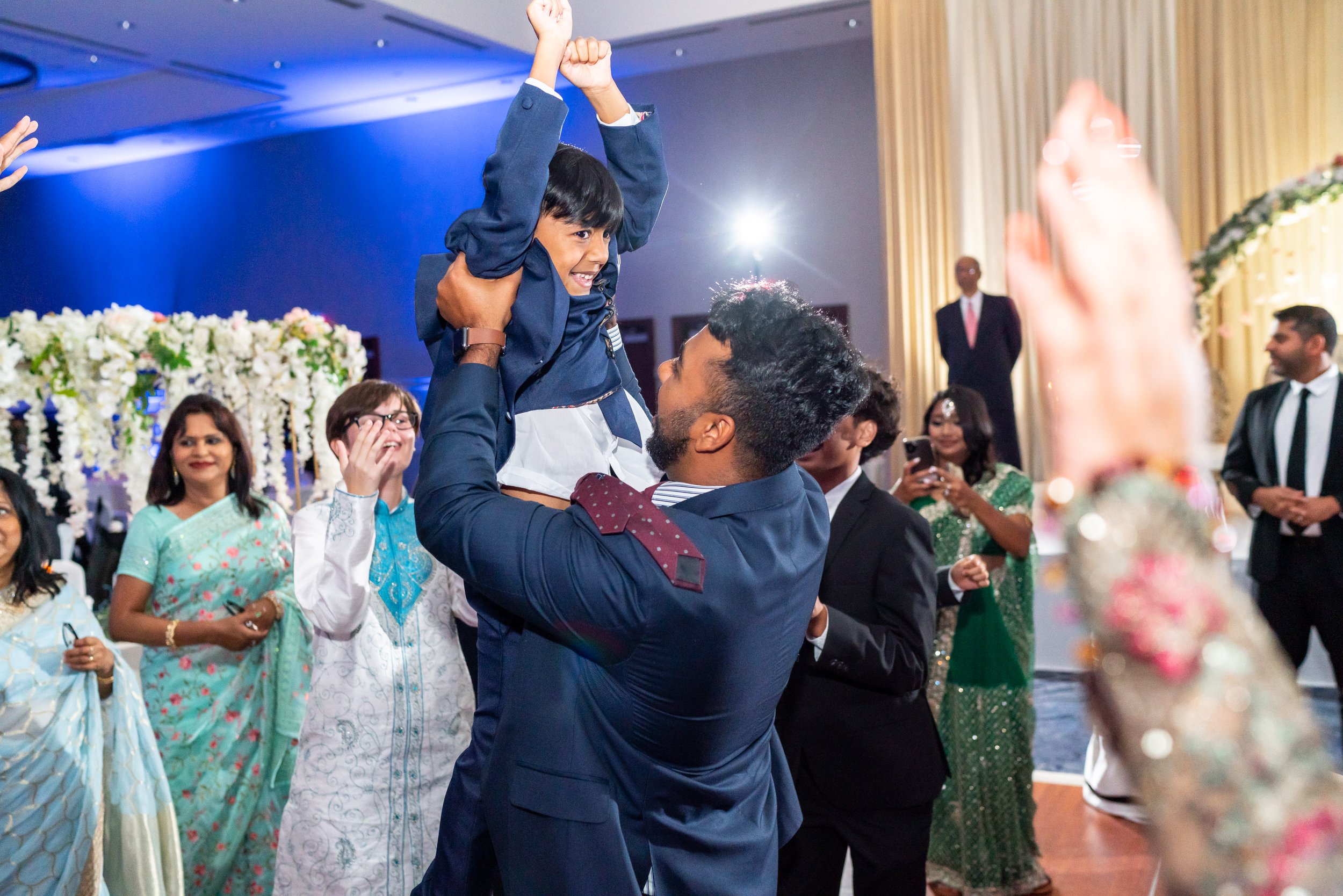 Wedding guest lifting his son on the dance floor at indian wedding