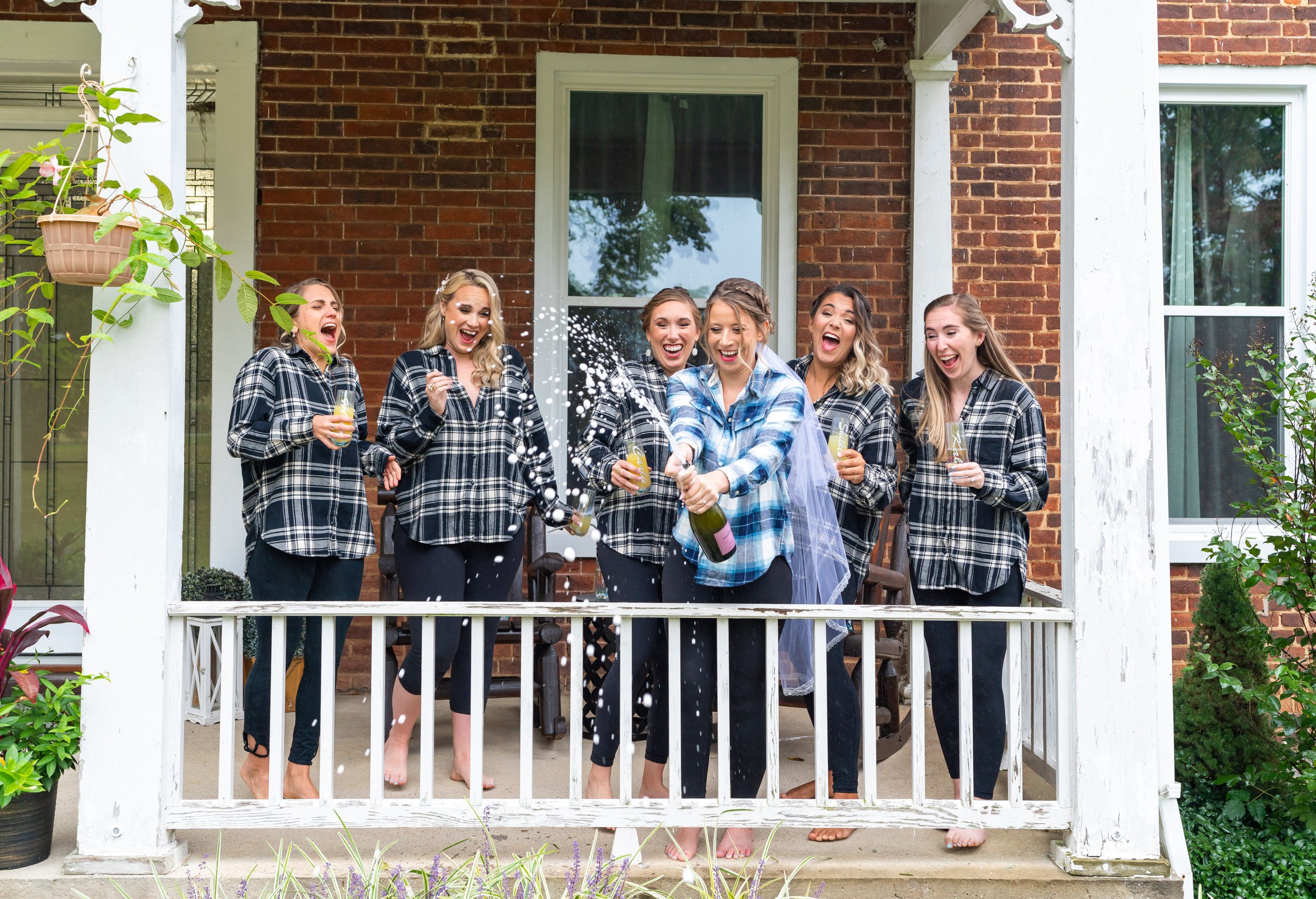 Bridesmaids and bride pop champagne on front porch of Stover Hall in Virginia