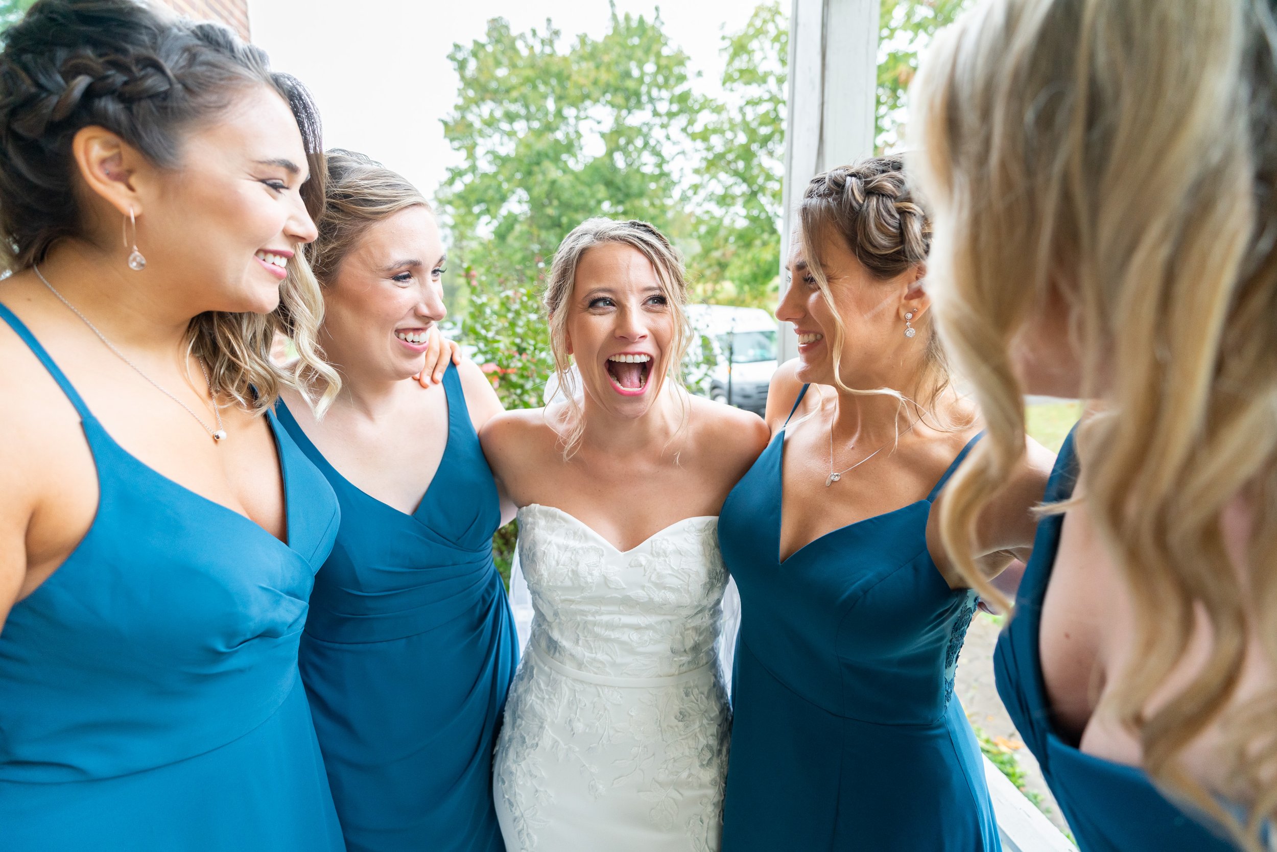 Bride laughing with bridesmaids in dark teal gowns from Amaze