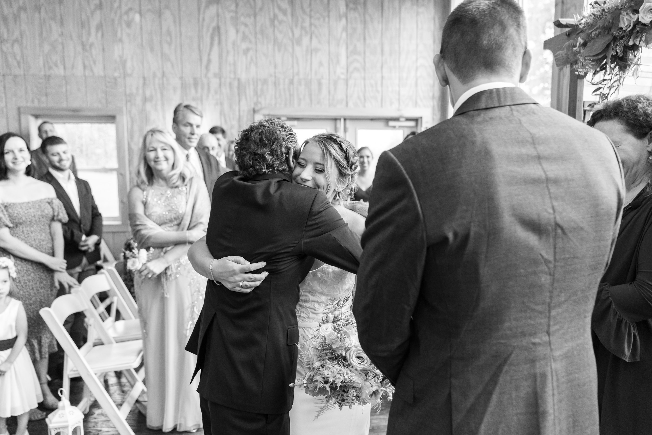 Bride hugs father while groom watches at Stover Hall