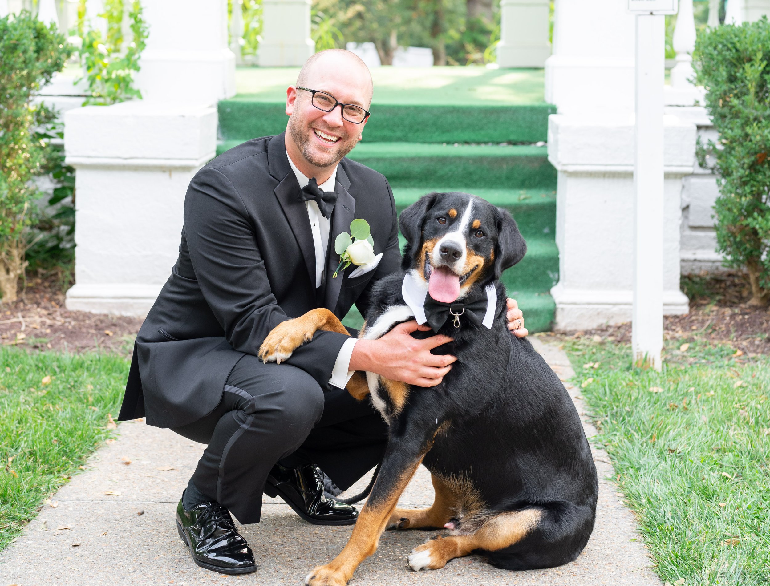 Groom sitting with his dog with paw over grooms arm in wedding tuxedo