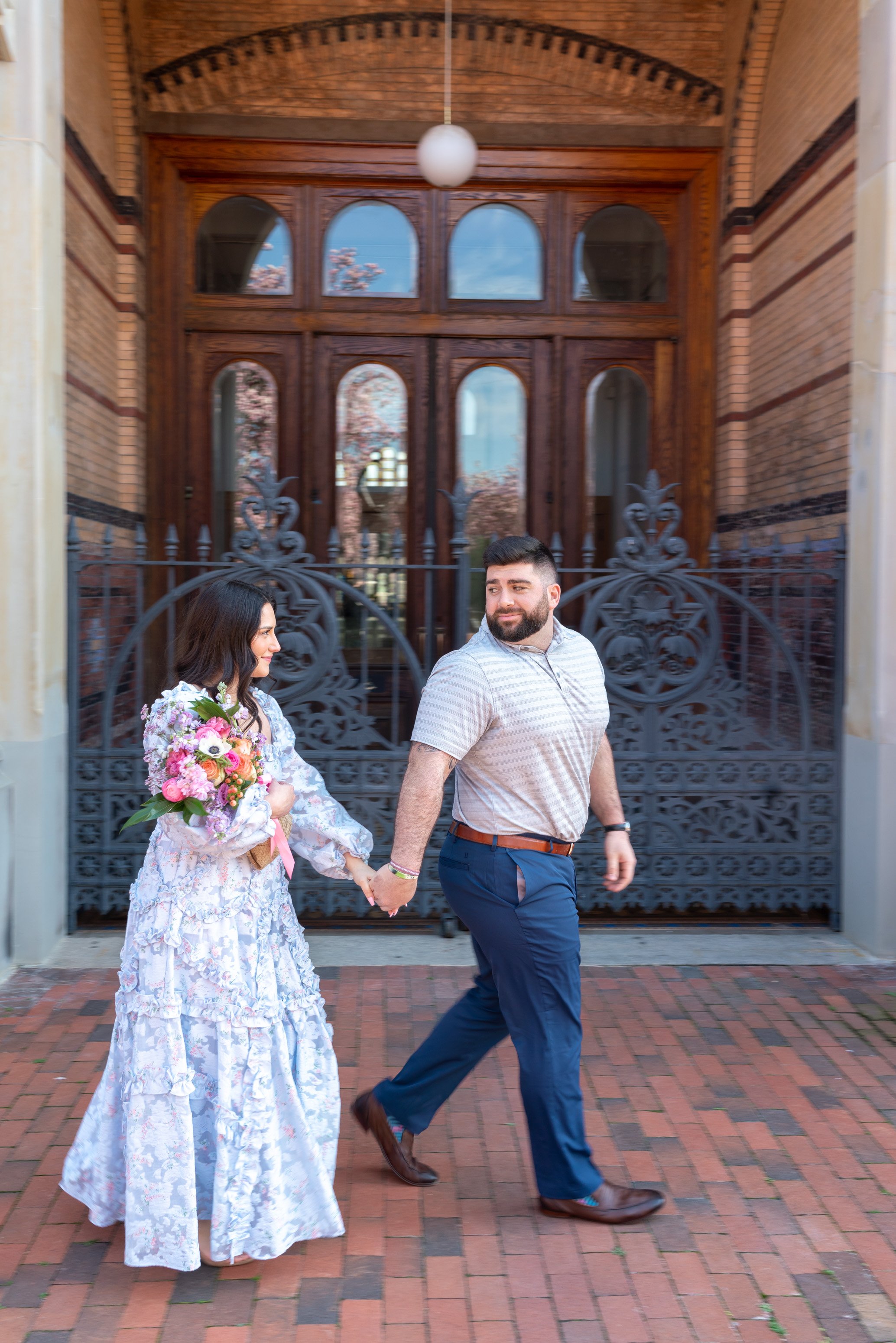 Bride and groom walk in front of iron gate at Enid A Haupt garden