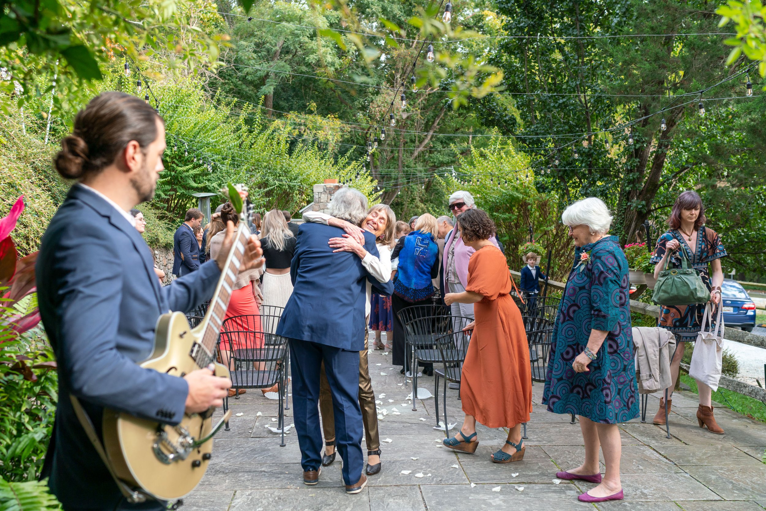 Guitarist plays music on terrace while guests hug and celebrate