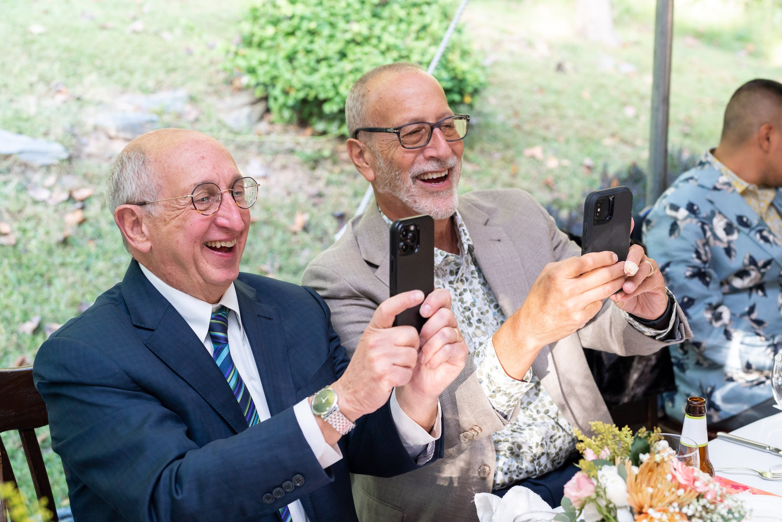two husbands taking an identical photo and laughing at wedding