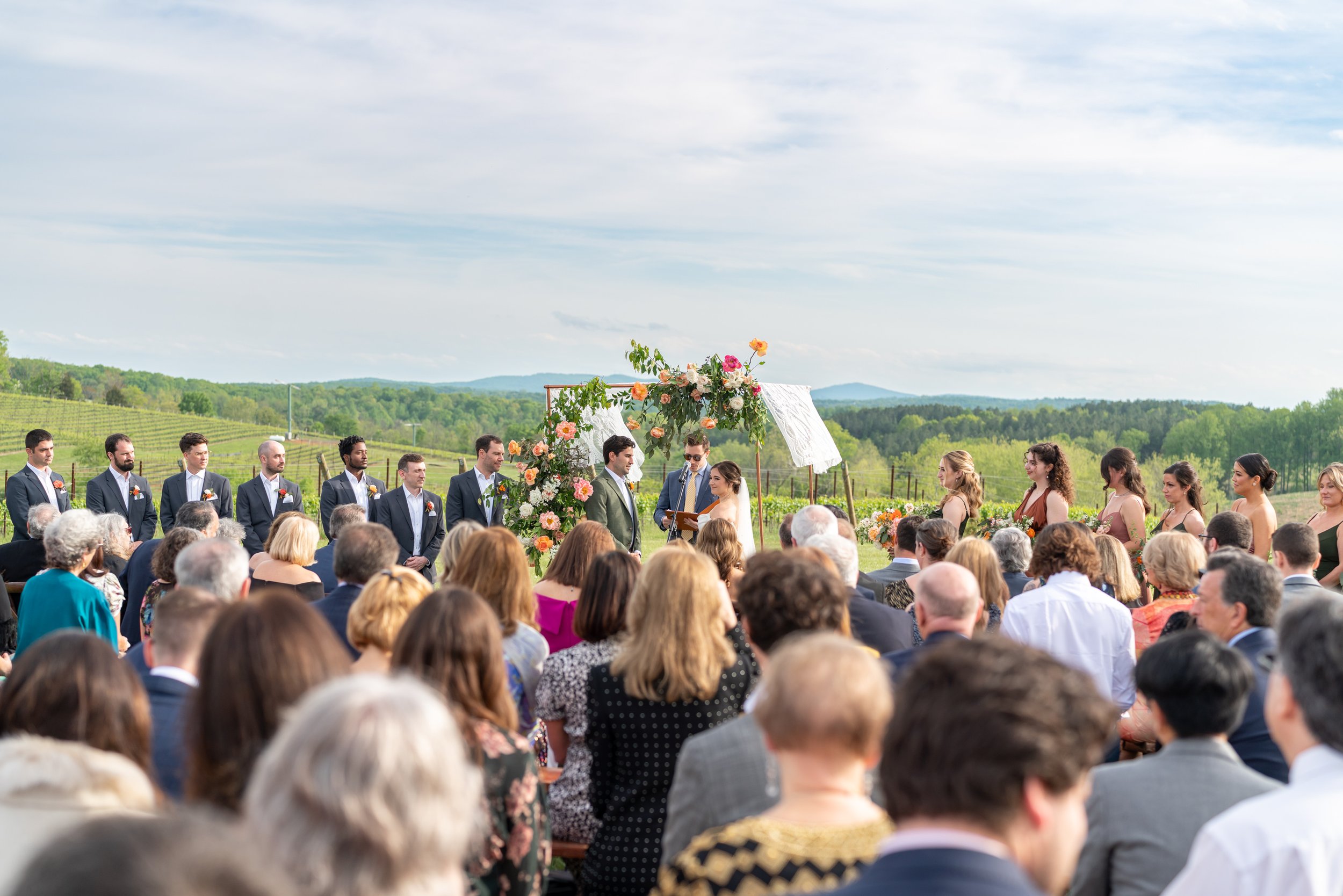 All the wedding guests watch the bride and groom under a copper floral arch