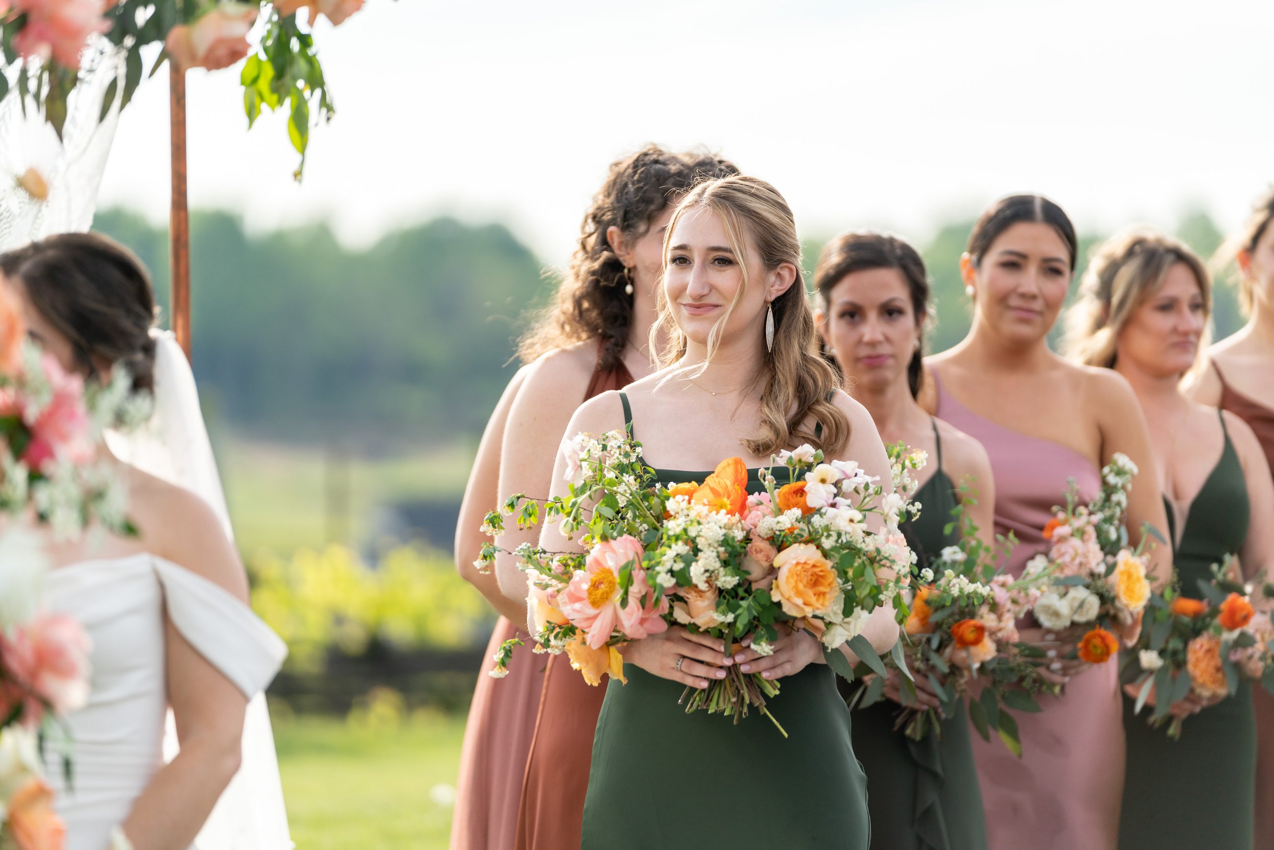 Maid of Honor and bridesmaids in copper, rose and green watch the vows