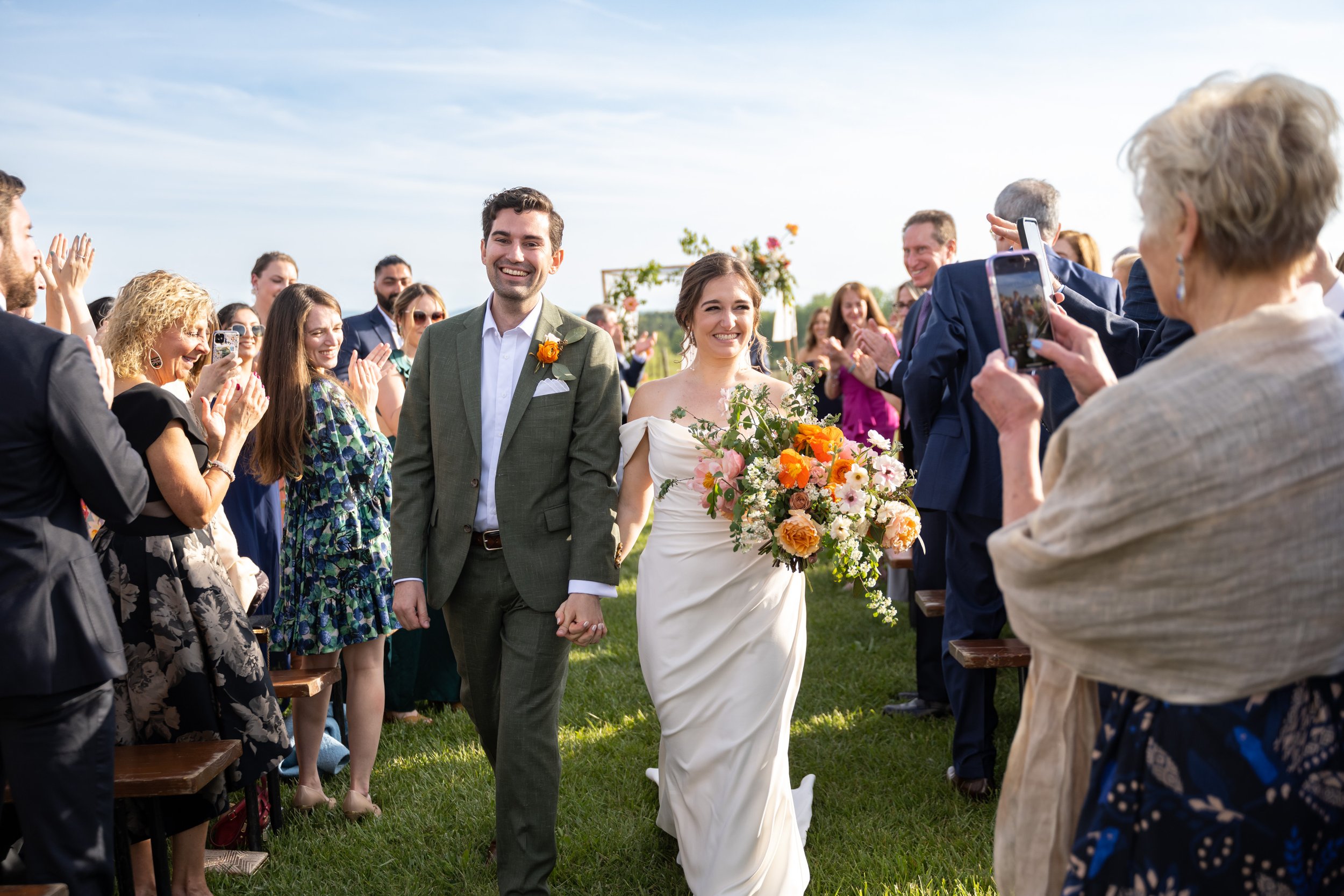 Bride and groom recess down the aisle with big smiles while guests clap