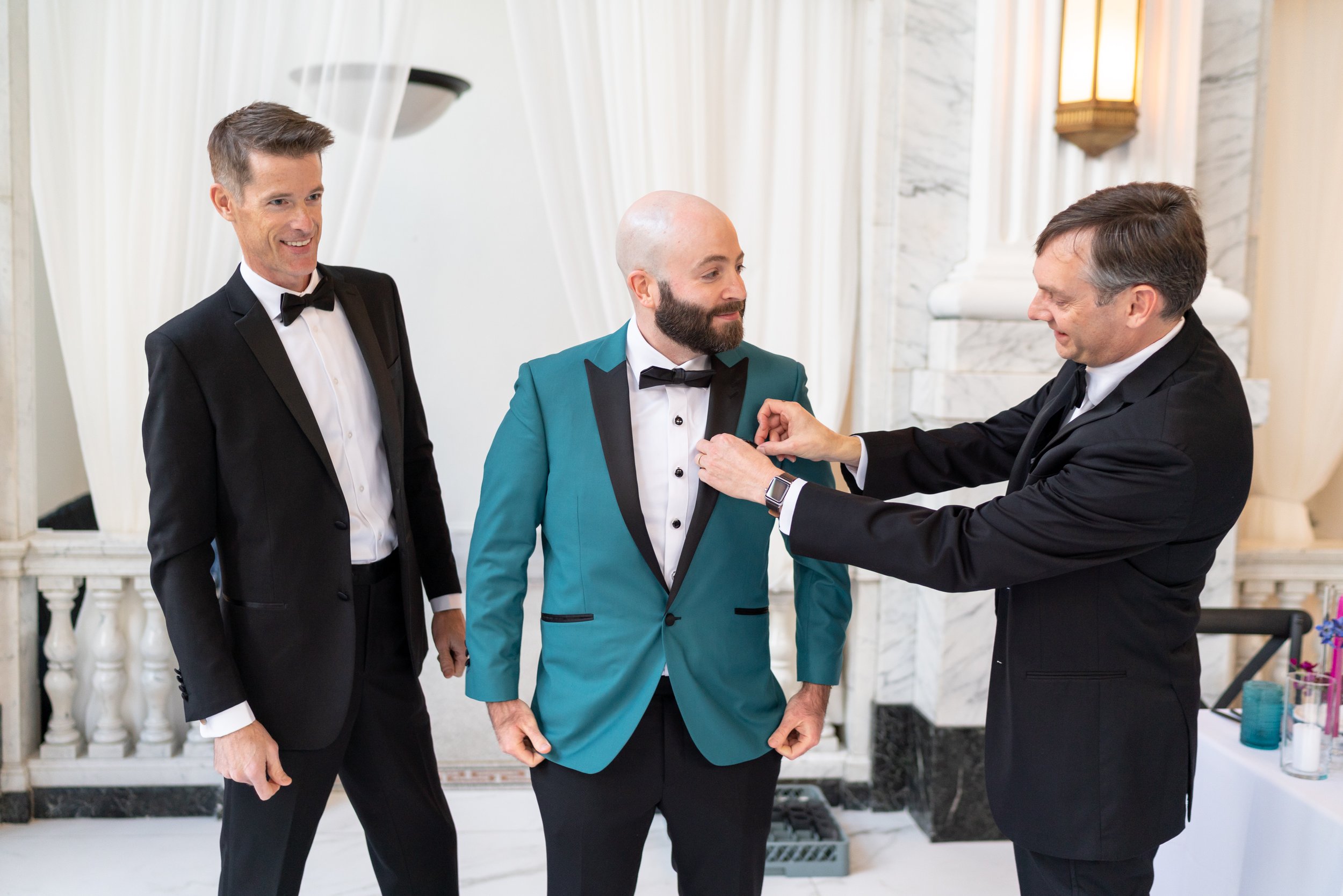 Groomsmen fixing groom's boutonniere at citizens ballroom bank