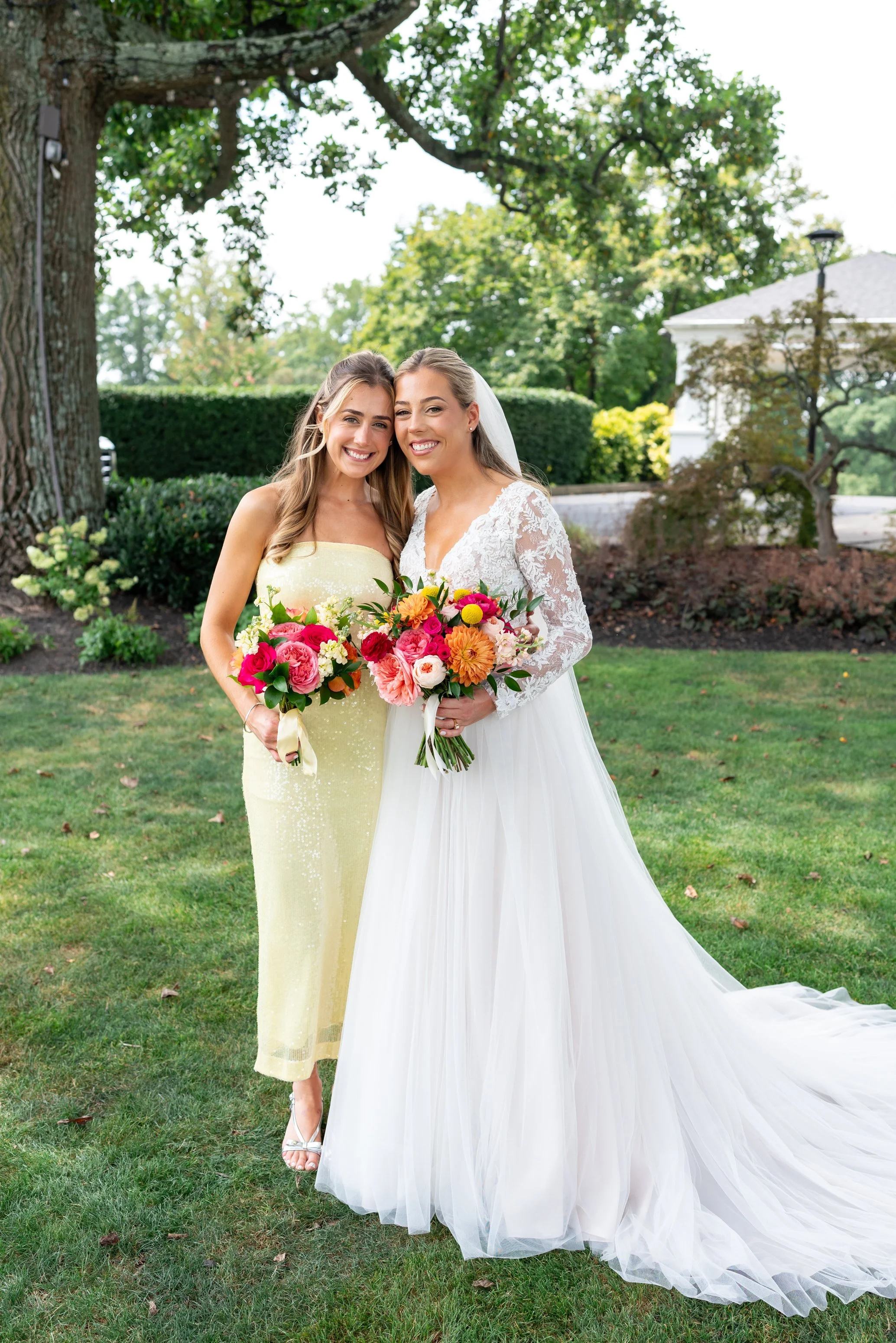 Bride poses with bridesmaid in yellow dress and colorful pink and orange flowers