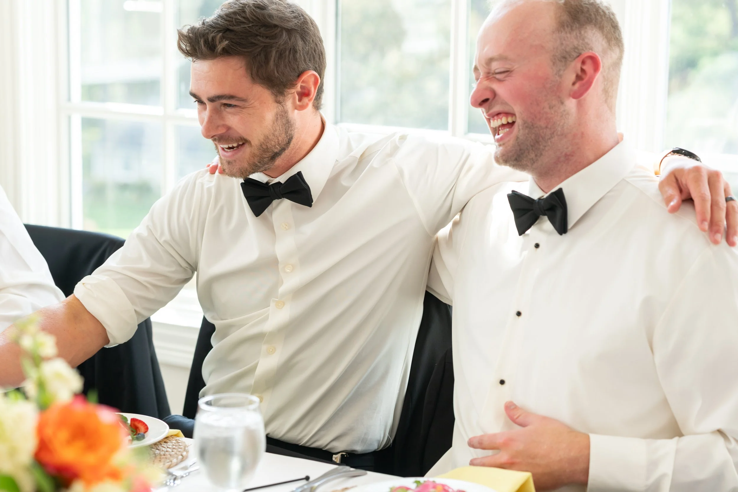 Groomsmen laugh at dinner reception space windows at Manor Country Club