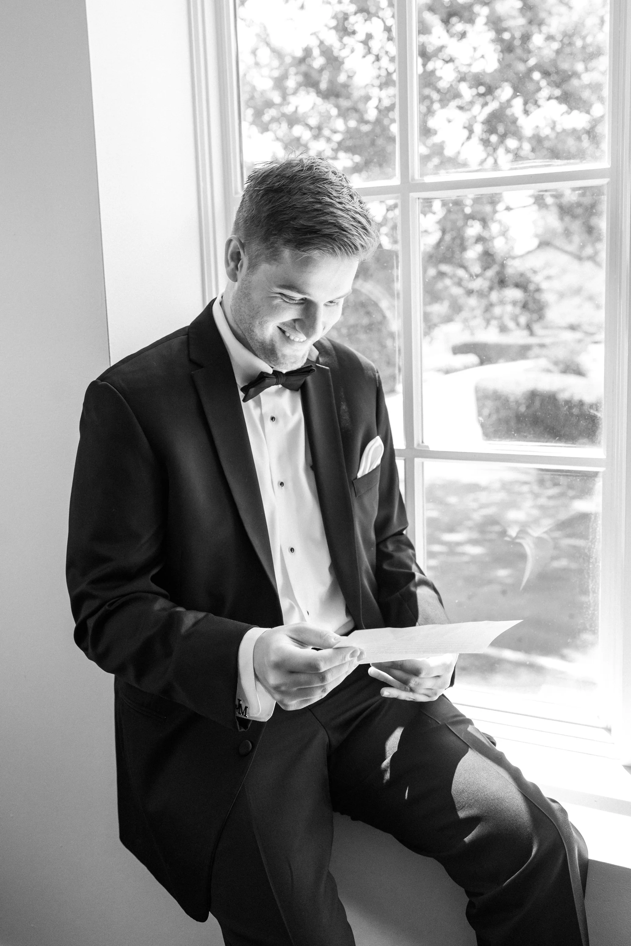 Groom reading letter from the bride sitting in the window at manor country club