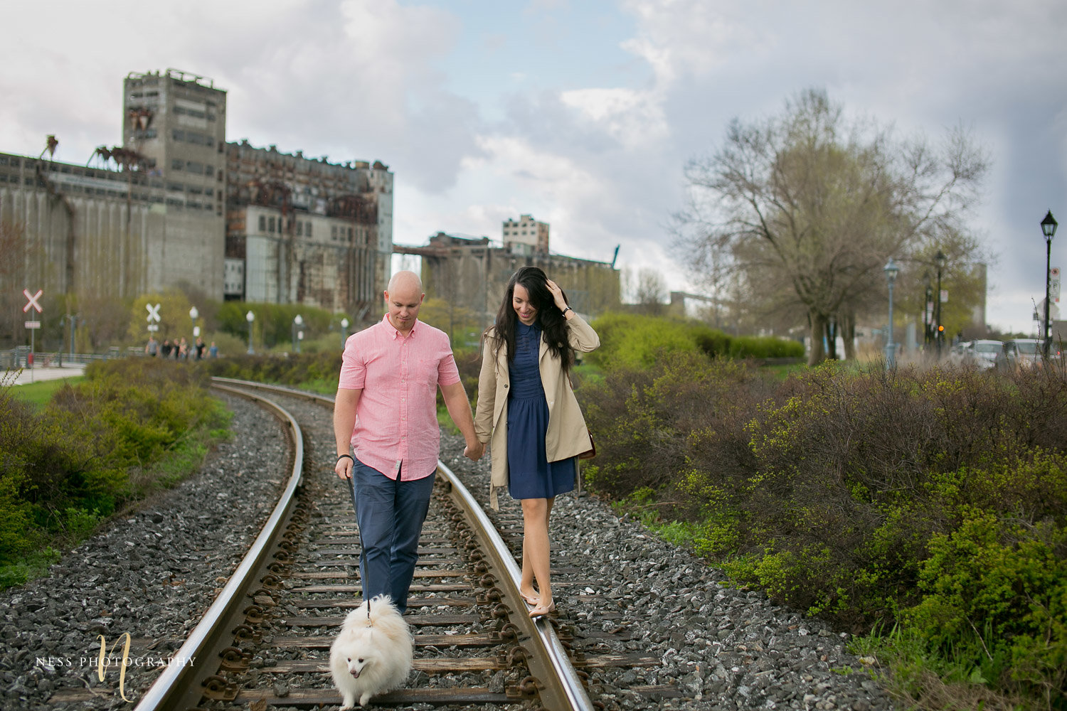 couple walking with their dog on train rails in the old port of montreal during engagement photo shoot