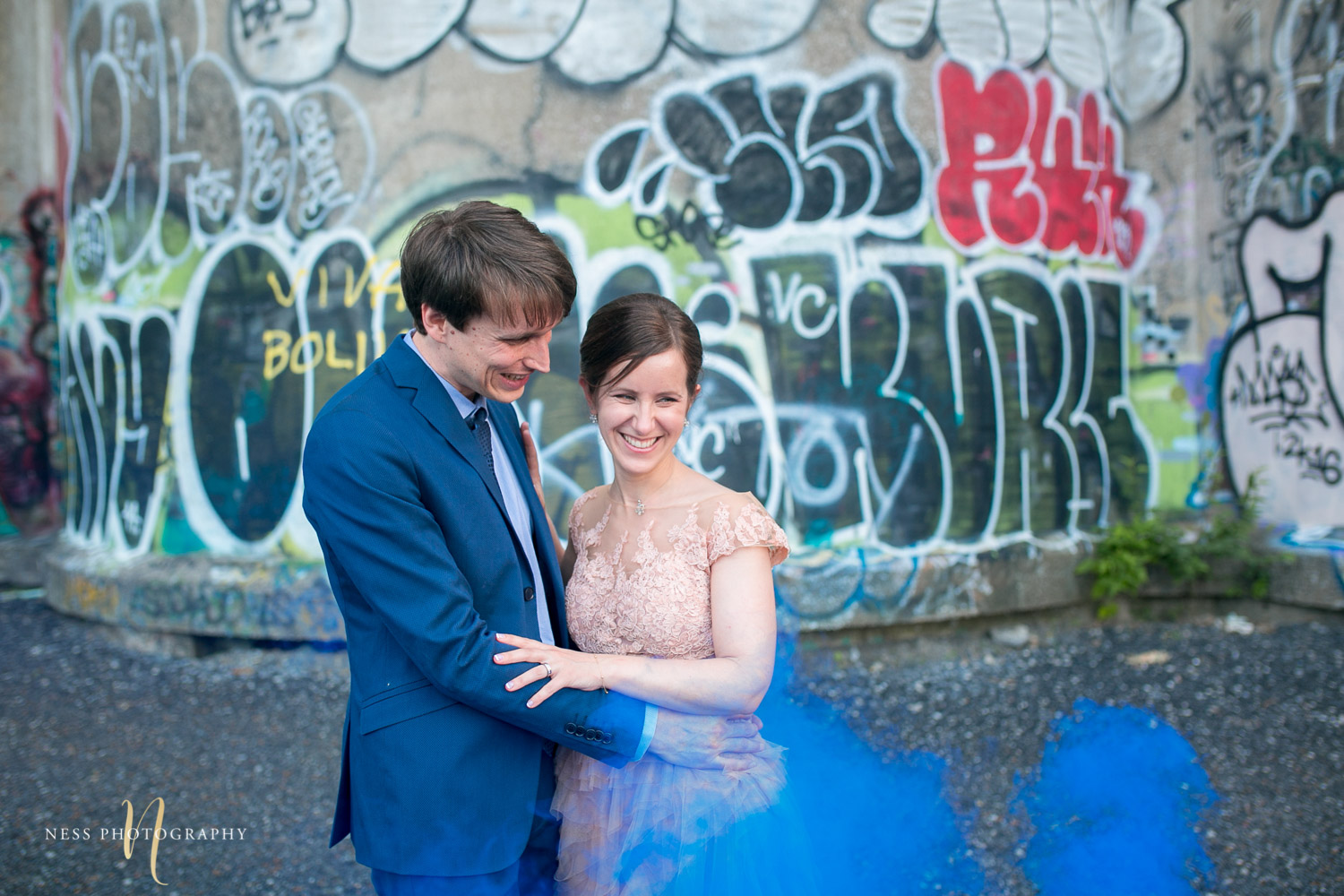 bride and groom in the middle of bleu smoke bomb in front of graffiti wall in canal lachine for their montreal elopement 