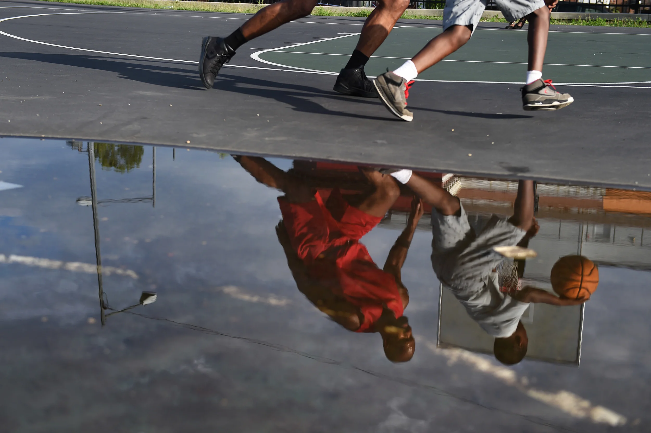  The reflection of DC native John Taylor, 52, left, &nbsp;and a neighborhood youngster is seen during a one-on-one basketball game at a Parkview neighborhood basketball court Tuesday, July 5, 206 in Washington D.C. &nbsp;(Photo by Christian K. Lee/Th