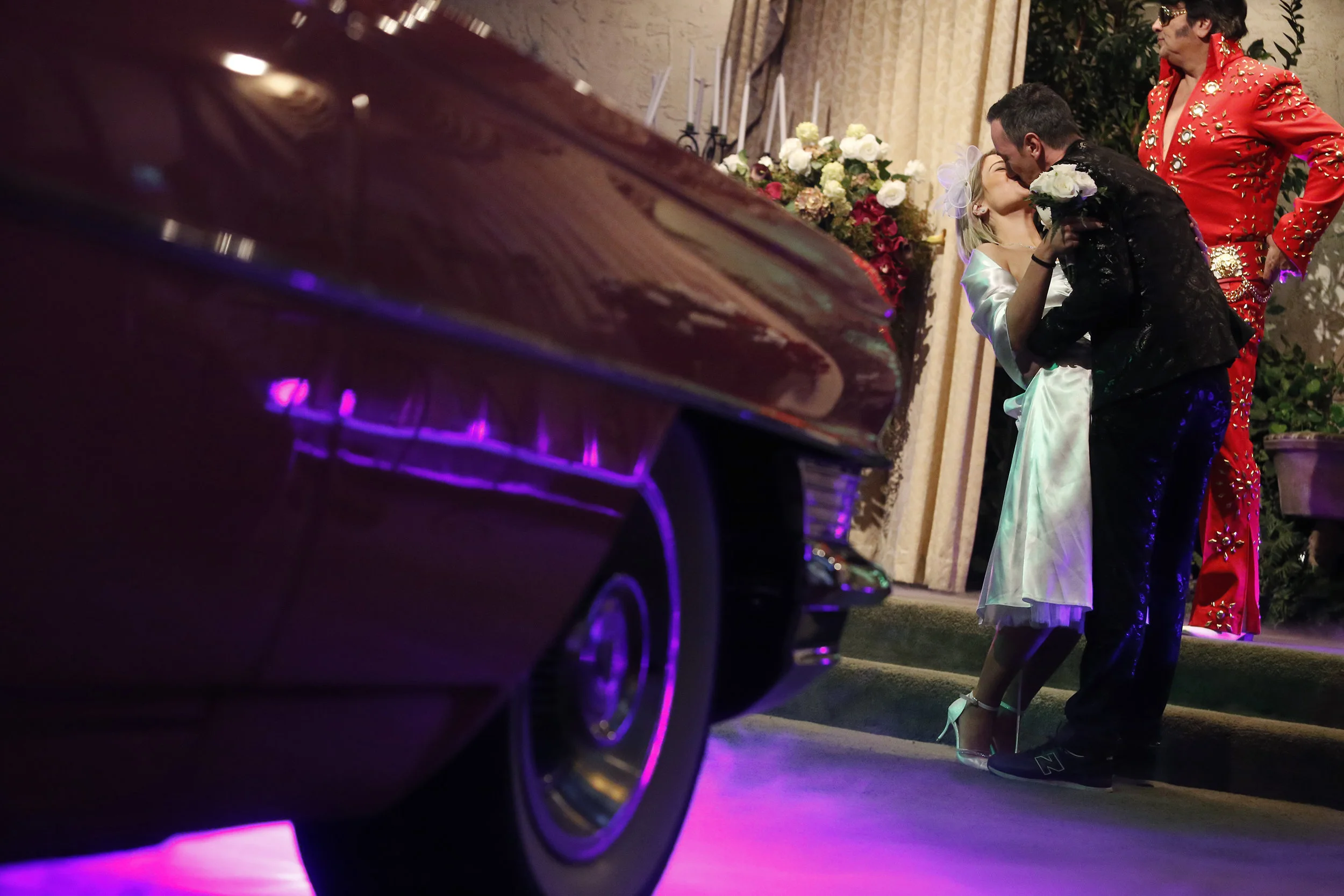  An Elvis impersonator looks uniterested as Celine Zind, left, kisses Frederic Spenle of Colmar, France in front of a pink cadillac during their Elvis themed wedding ceremony inside the Viva Las Vegas Wedding Chapel on Valentines Day 2017, in Las Veg