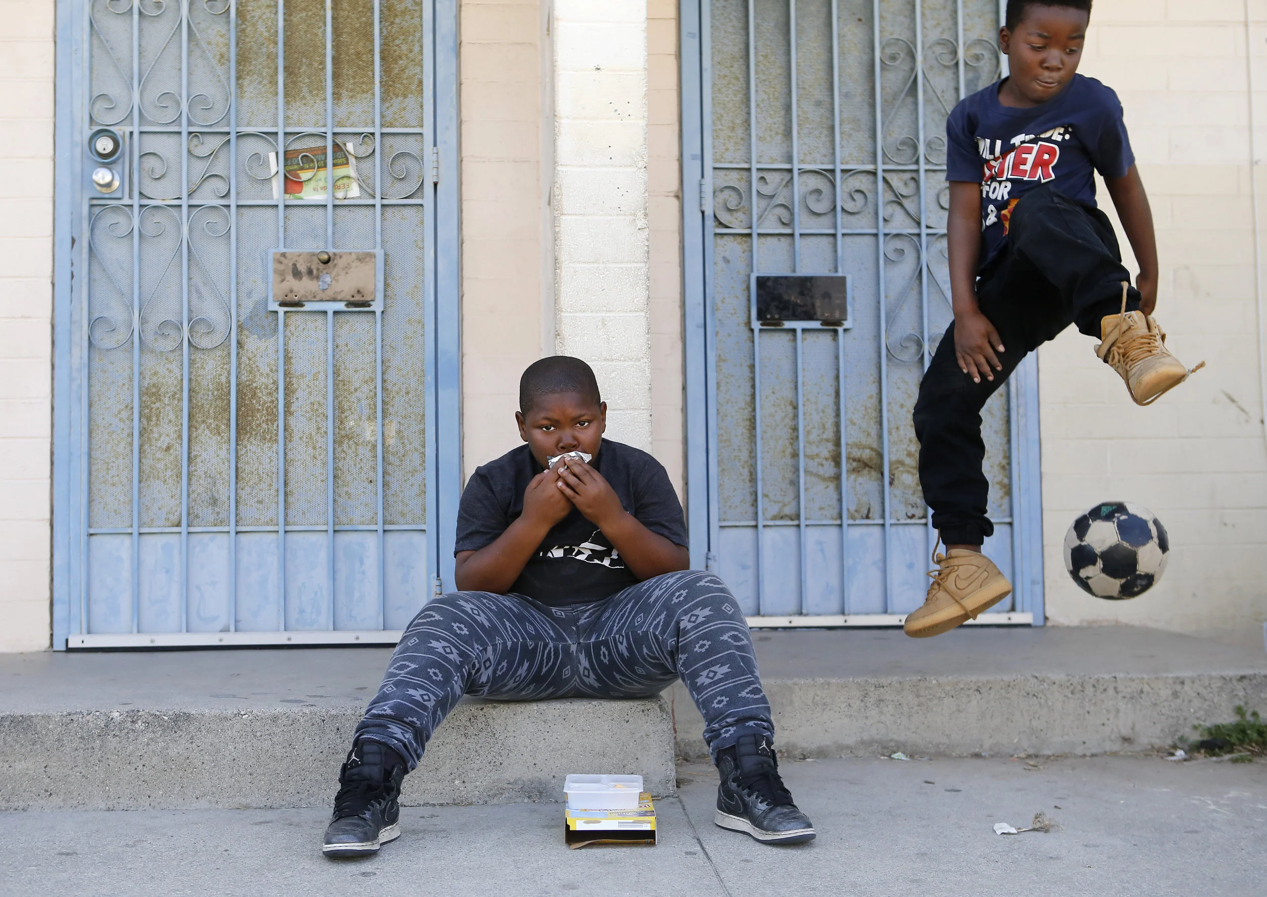  Demarion Washington, 8, from left, drinks his juice in front of his home as Justin Scott, 8, leaps from a porch at the Jordan Downs Housing Projects in Watts, CA on Monday, June 5, 2017. (Christian K. Lee/ Los Angeles Times) 