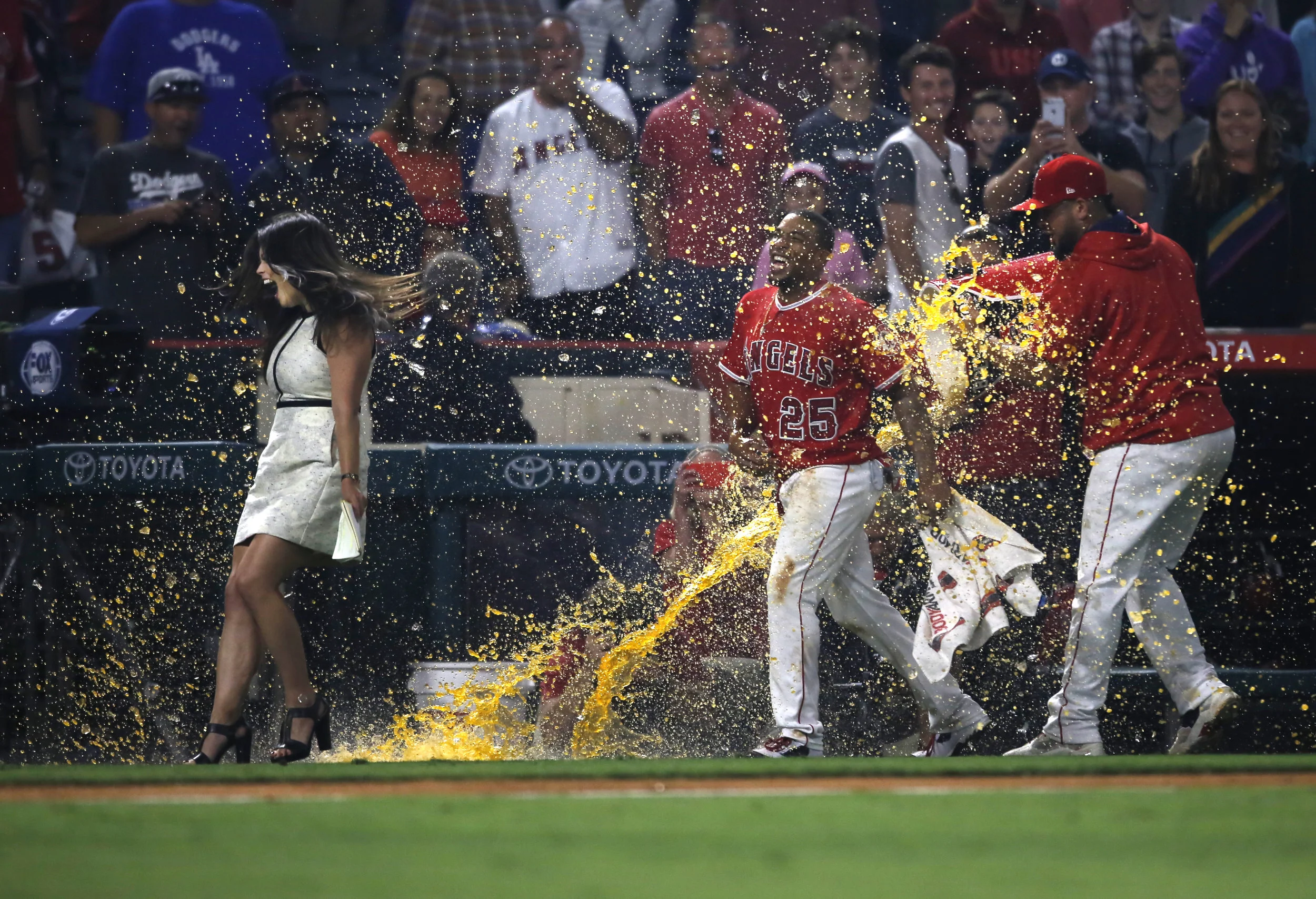  Fox Sports announcer Alex Curry, left, reacts as Los Angeles Angels left fielder Ben Revere (25) is splashed with liquid after winning a Major League Baseball game against the Los Angeles Dodgers at Angel Stadium of Anaheim in Anaheim, CA on Wednesd