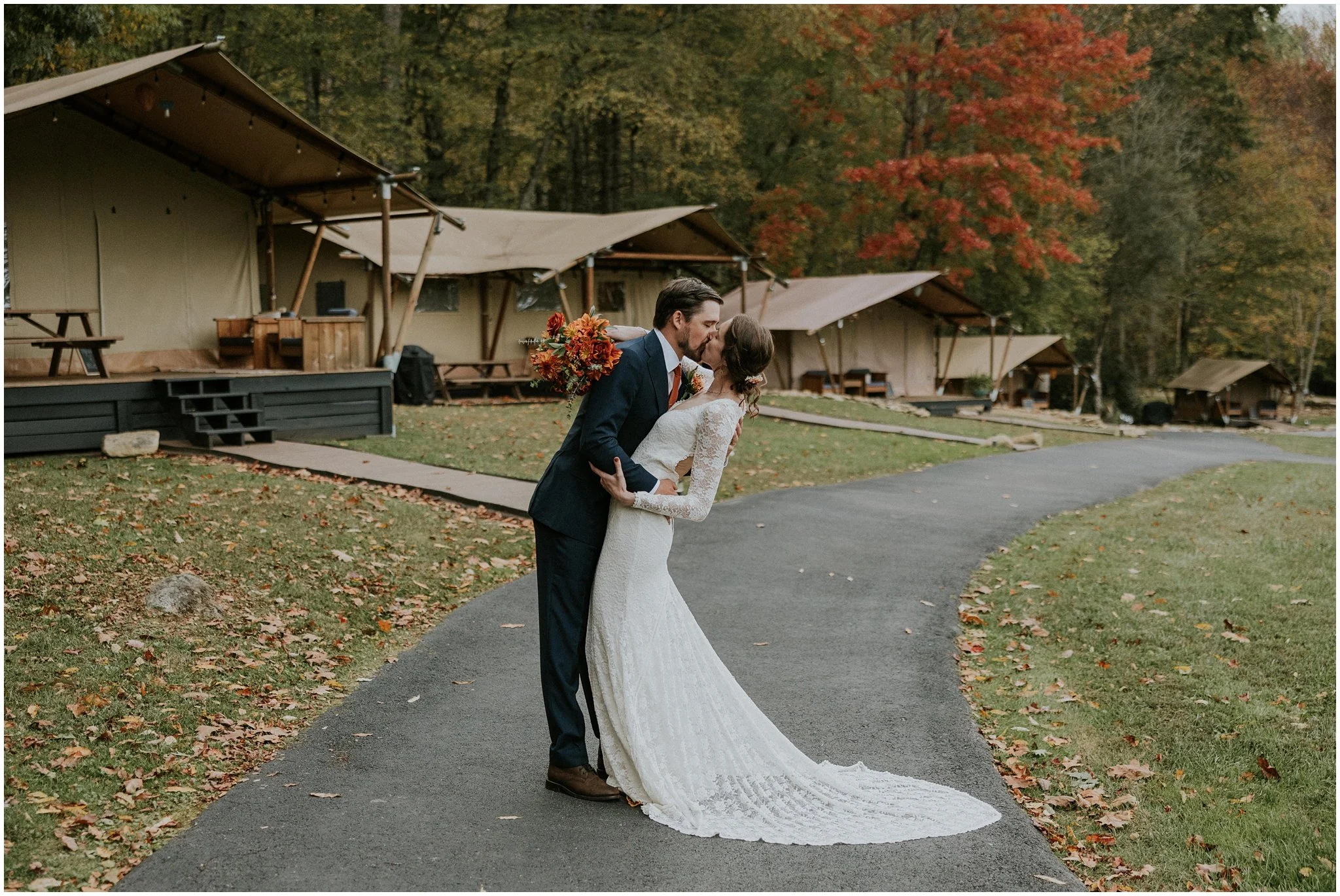 A bride and groom share a kiss on a pathway near a row of canvas tents in the mountains at Glamping Retro in Erwin, Tennessee.