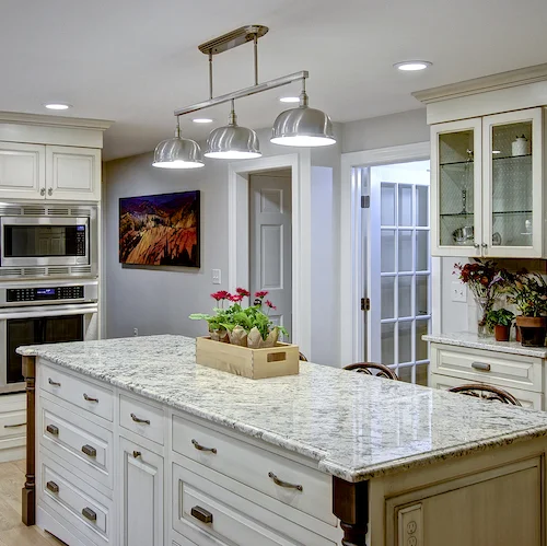 A New Traditional kitchen featuring an island with furniture-style details, intricate elements, and a school house light fixture.