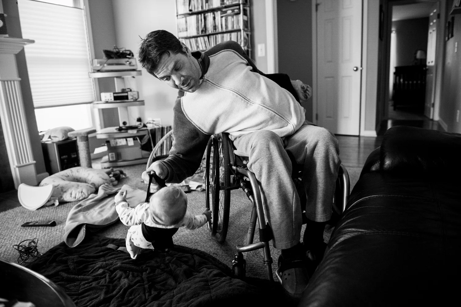 David lifts his son, Duncan onto his lap to put him down for a nap. Since David only has use of his right arm, which is weak he has created a device to lift Duncan up and down carefully to help. He worries when his son is over 25 pounds, he might not be able to lift him.