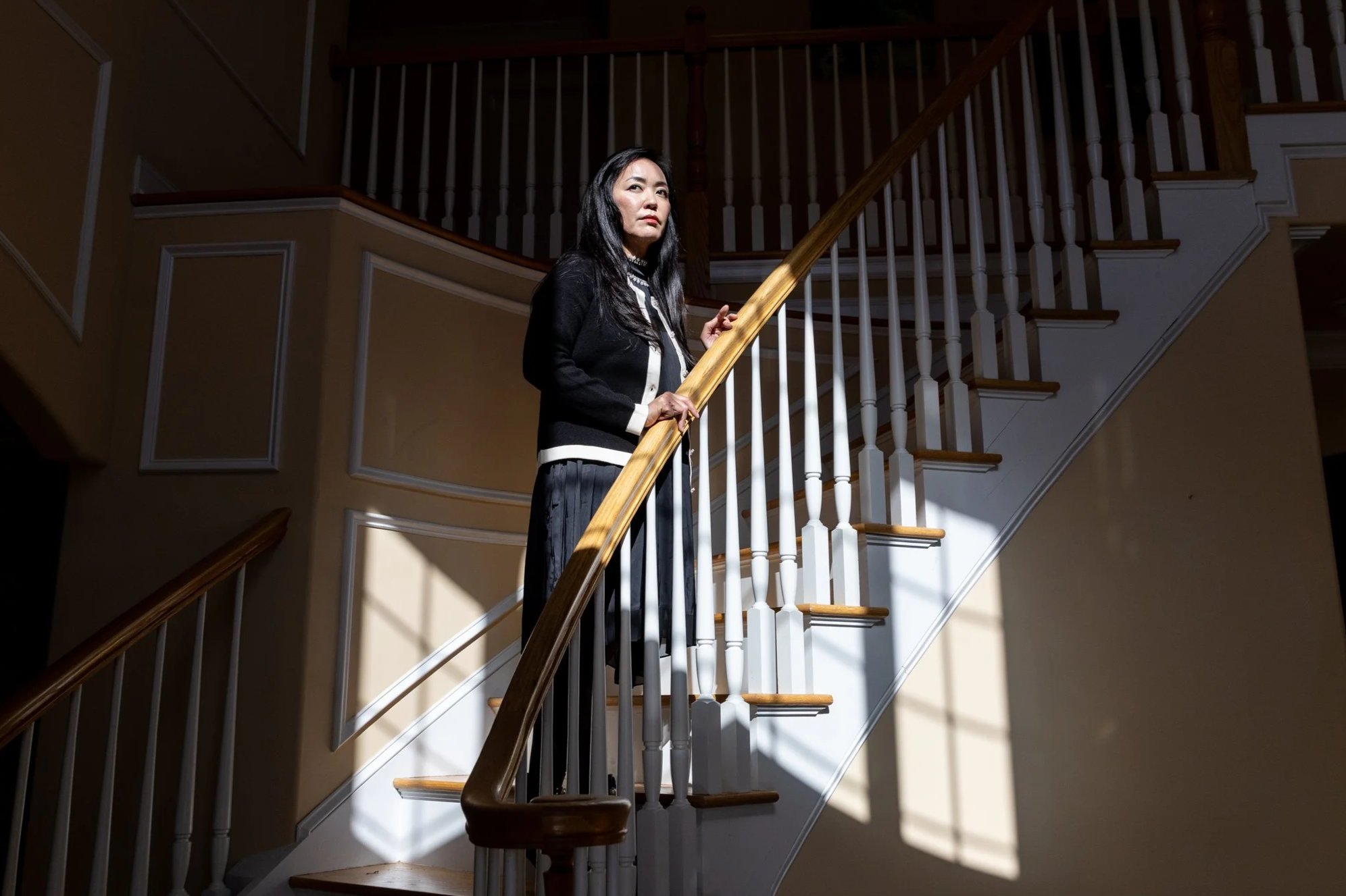 A survivor of Jeffery Epstein standing on a staircase, illuminated by sunlight, inside her house.