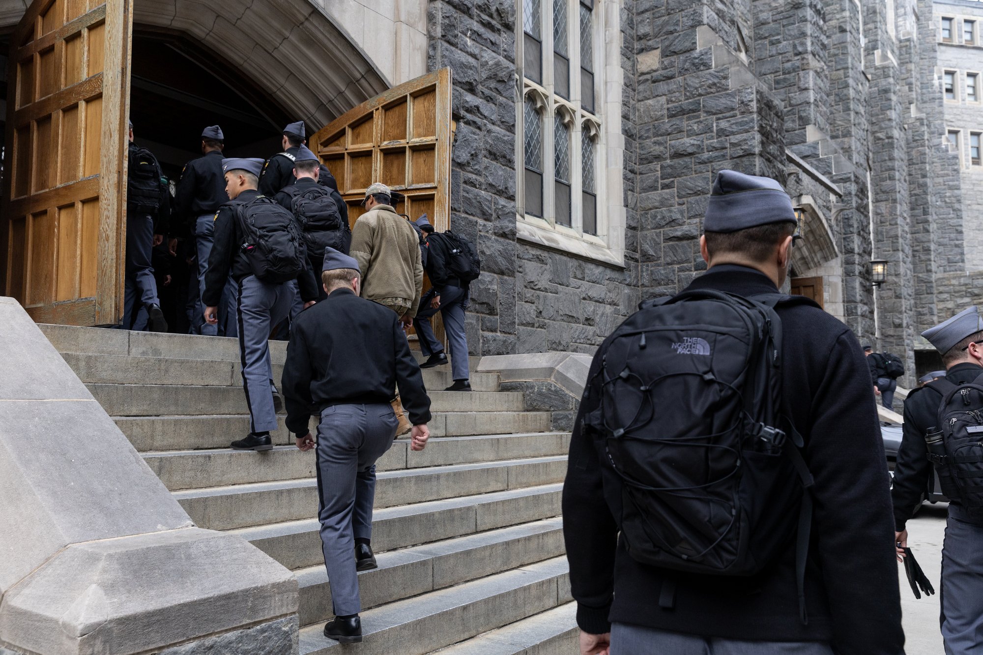 A group of police officers and a man walking up the steps of a large stone building with gothic windows, possibly a courthouse or government building.