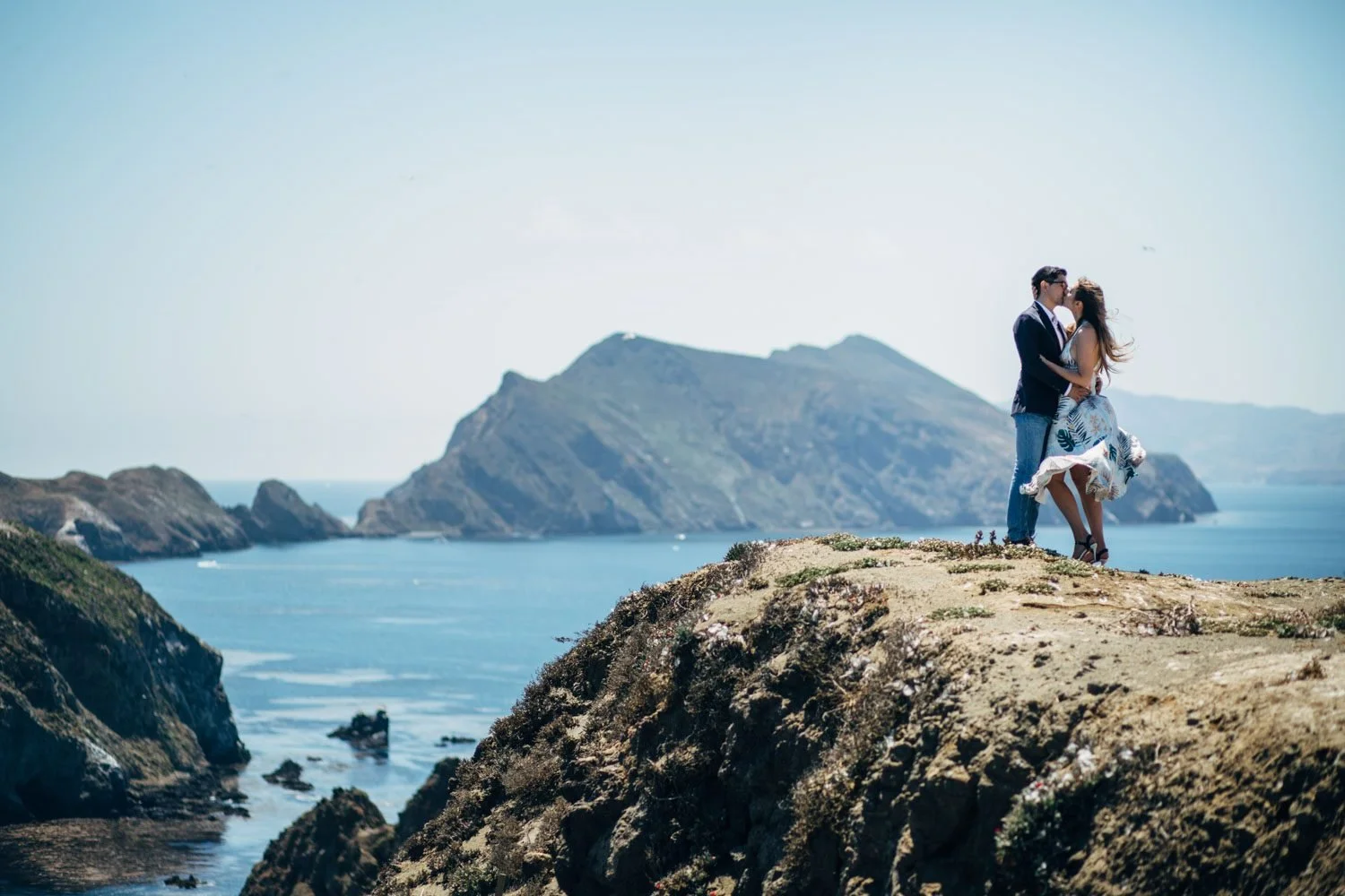 Couple kissing on an Anacapa Island clifftop at Channel Islands National Park, with dramatic rocky peaks and deep blue ocean filling the background