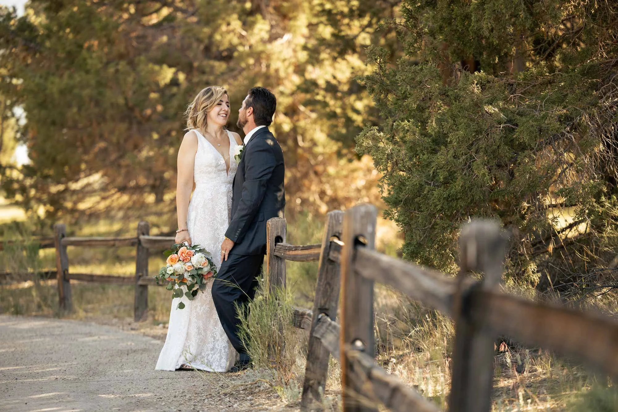 Bride and groom smiling on a dirt path beside a rustic fence at golden hour in Big Bear CA (Copy)