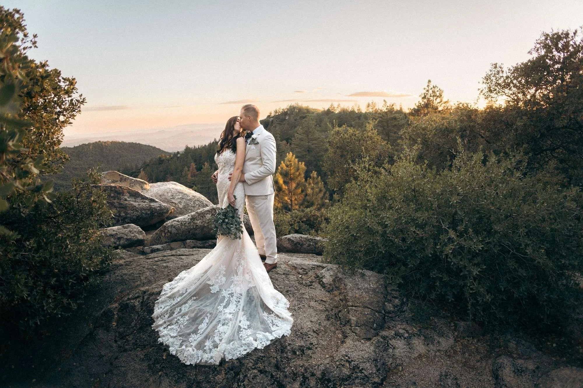 Bride in lace gown kissing groom on a rocky hillside at sunset in Idyllwild CA (Copy)
