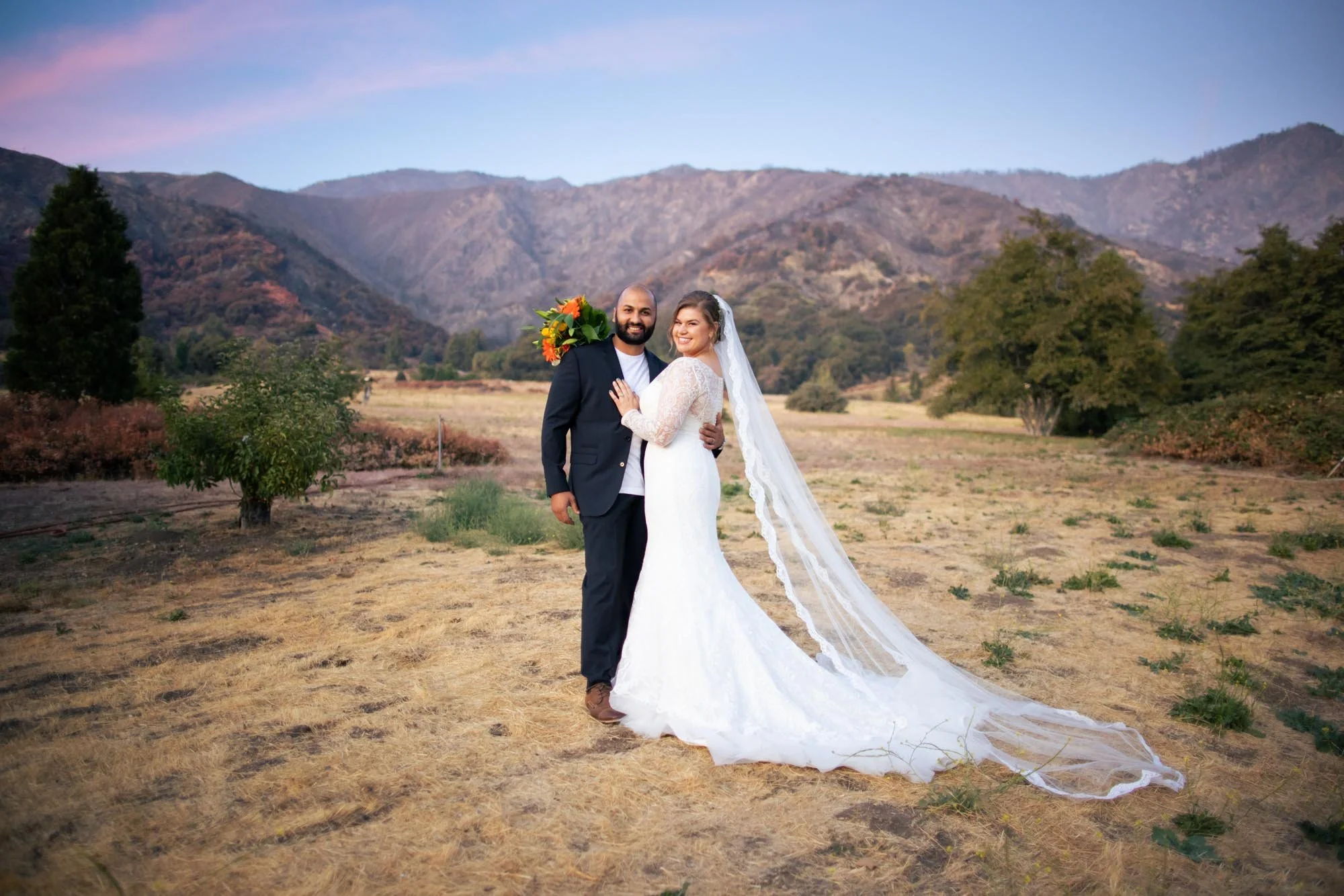 Bride with cathedral veil posing with groom in a mountain valley at sunset in Oak Glen CA (Copy)