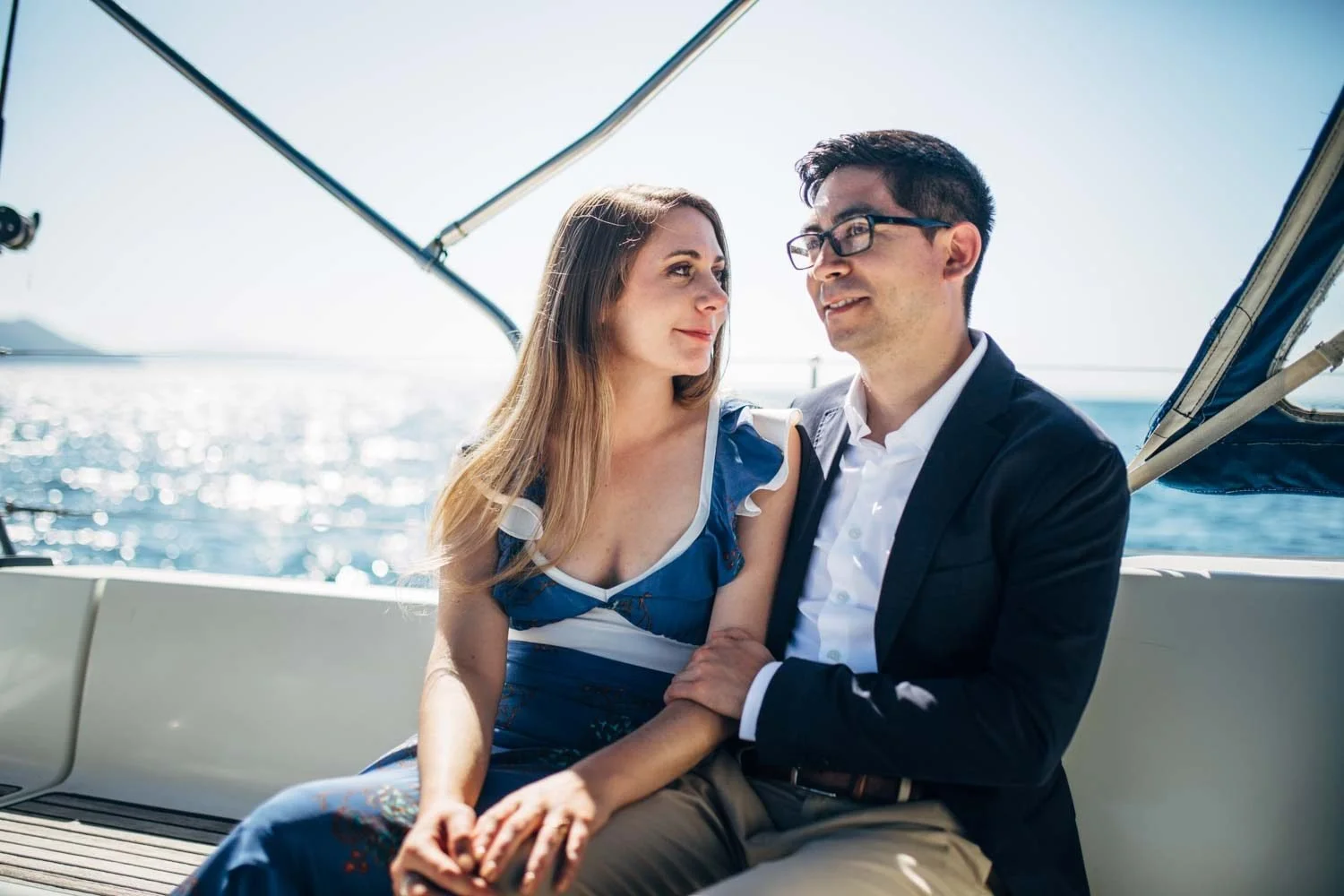Engaged couple sitting close together on a sailboat deck near Anacapa Island, Channel Islands National Park, with sparkling blue ocean stretching behind them