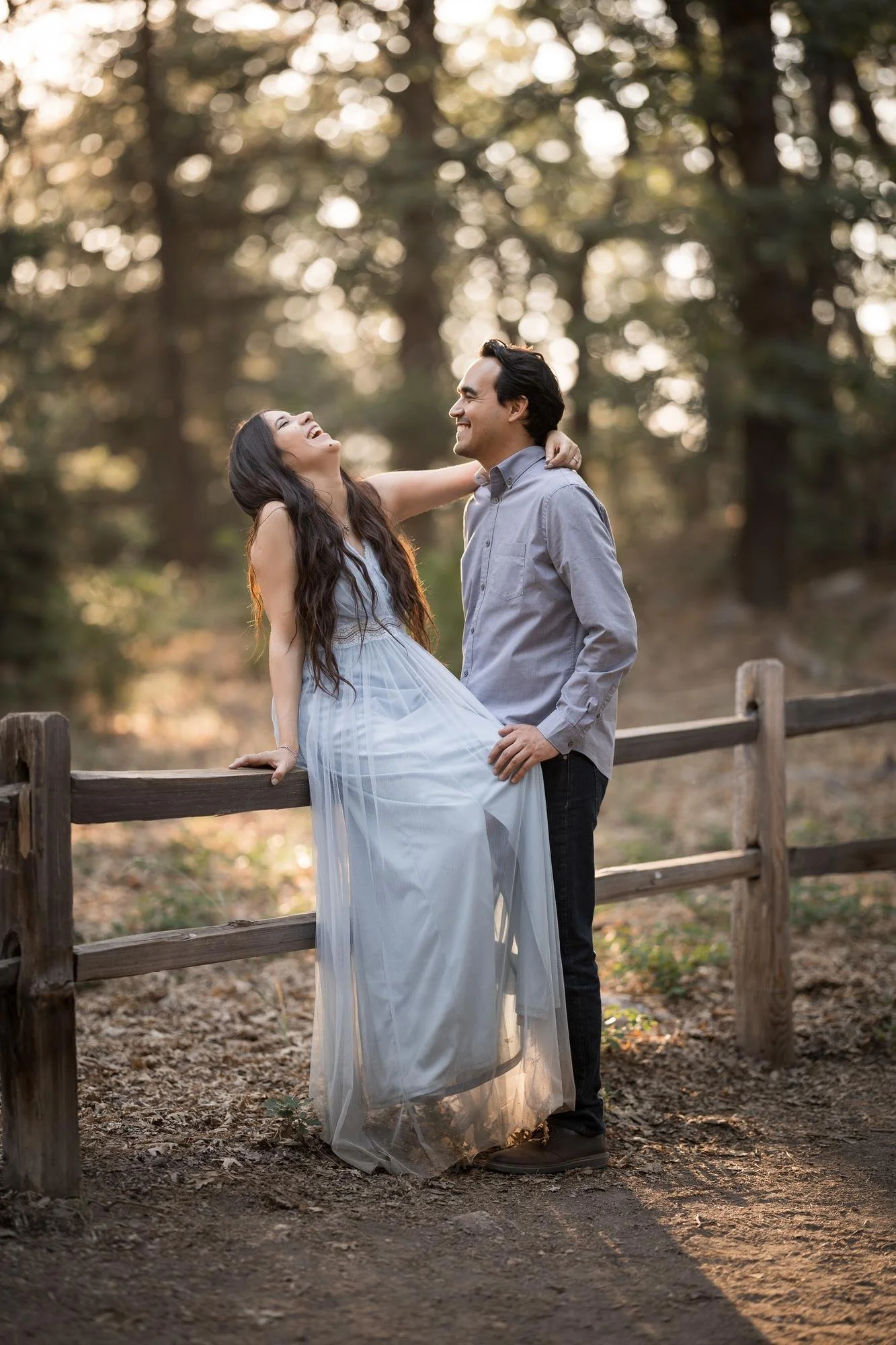 Couple laughing together by a rustic wooden fence at Heaps Peak Arboretum in the San Bernardino Mountains during warm golden hour engagement portraits