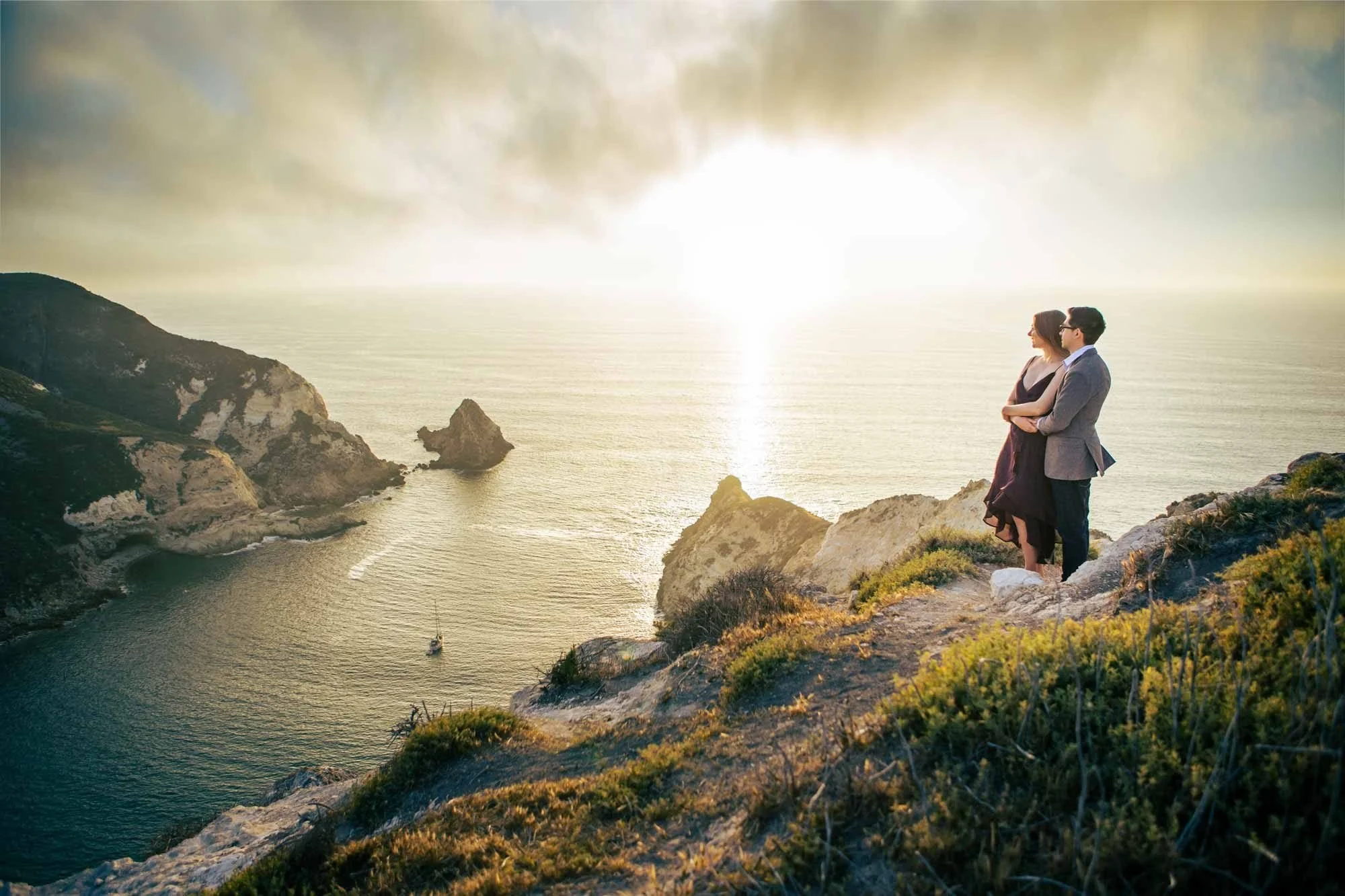 Couple embracing on a Channel Islands cliffside overlooking the ocean and sea stacks during a glowing golden sunset