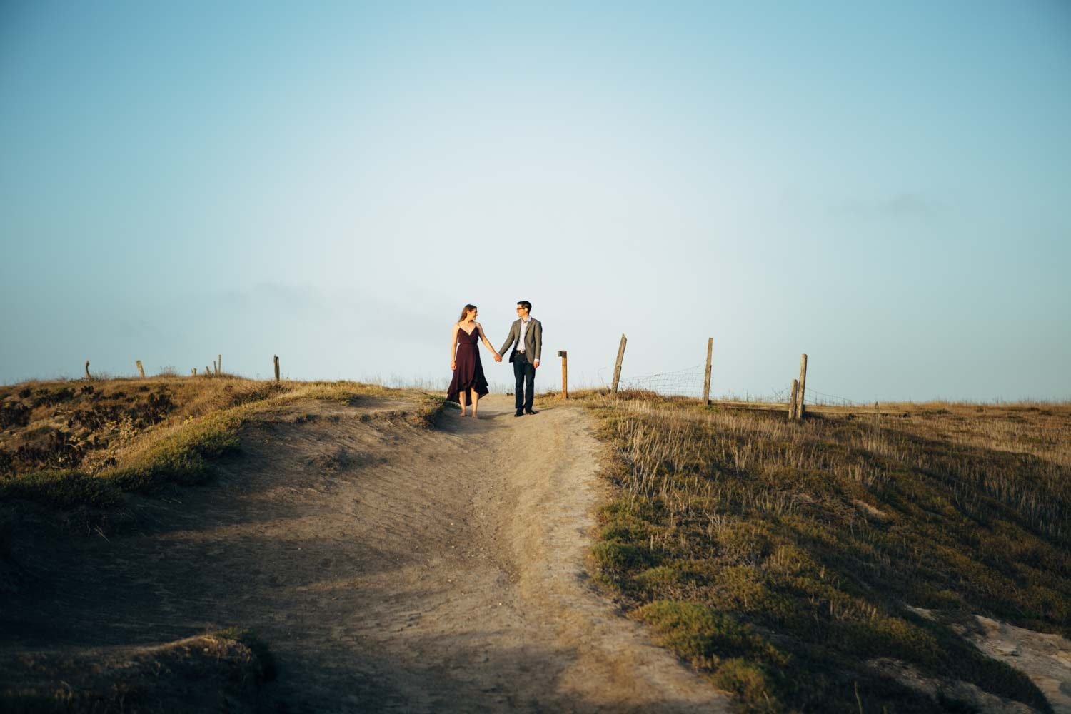 Couple holding hands on a golden coastal hilltop trail at Santa Cruz Island, Channel Islands National Park, with a wide open blue sky above them