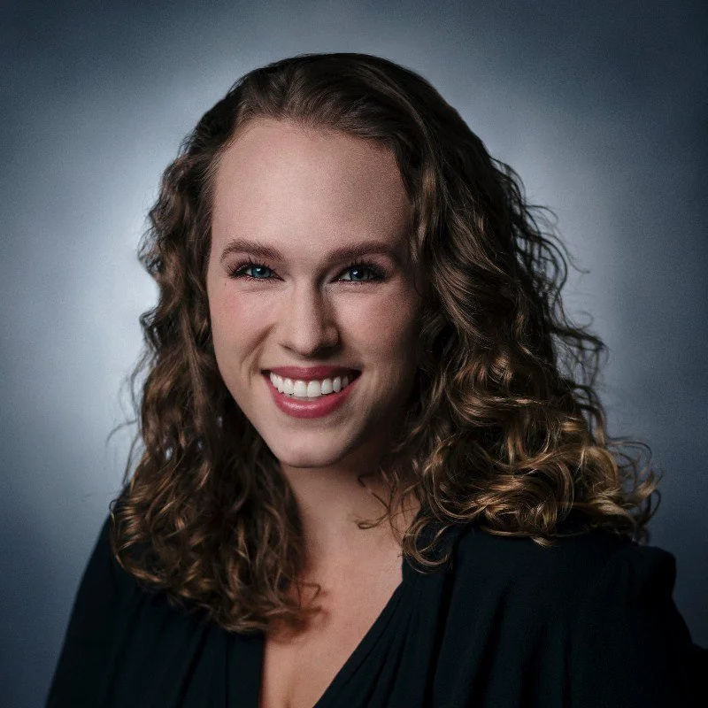 A woman with curly hair smiling against a dark background.
