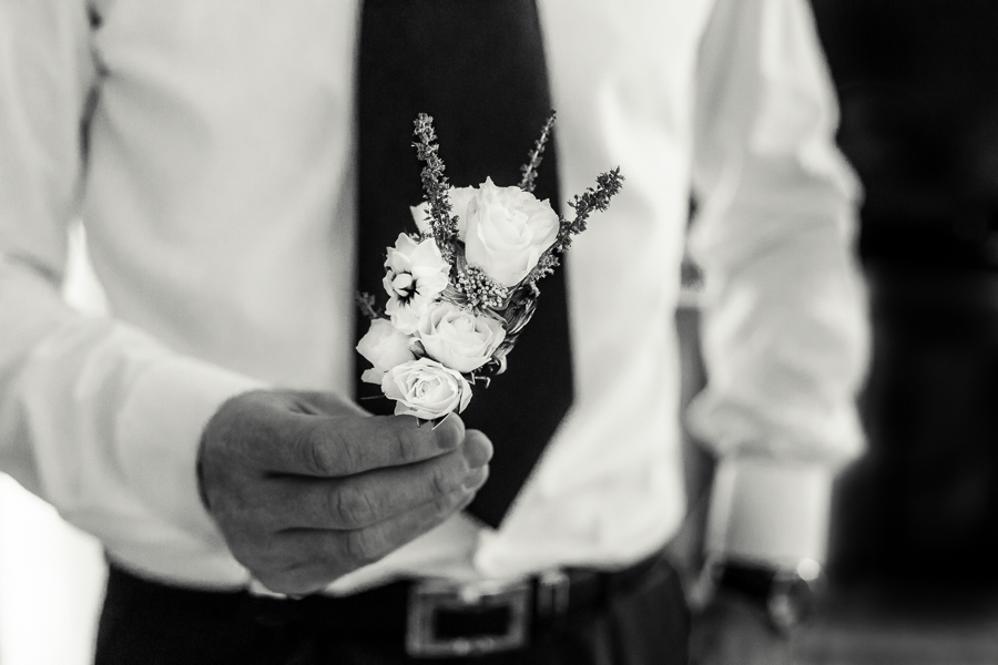 the hands of groom holding his boutonnière 